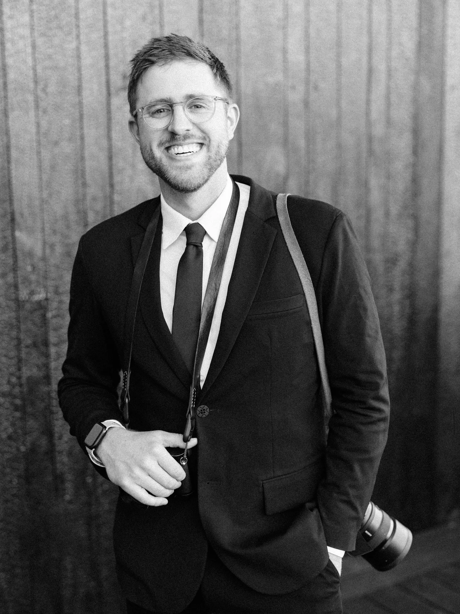 Grant Daniels smiling in a dark suit with his camera on a leather strap