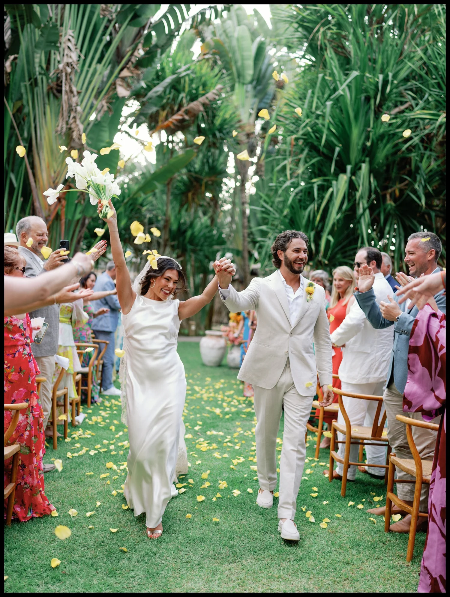 A couple walking out through a lush garden as guests cheer
