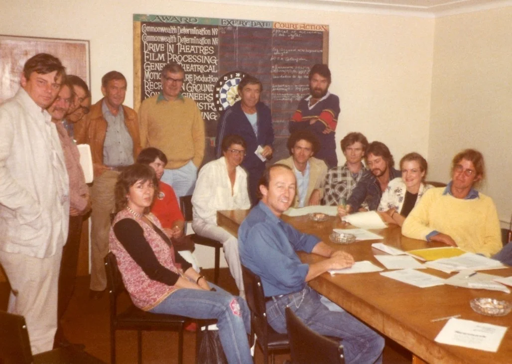 A photograph was taken at the meeting in 1981 to set up the original articles of Association. From left to right: (Standing) Michael Thornhill, Albie Thoms, Richard Michalak, Eric Gross, John Power, David Baker, Michael Pate, Bert Deling. (seated) Tom Jeffrey, Linda Blagg, Di Drew (in red), Henri Saffron, Tom Cowan, Chris Noonan, Ian Barry, Gillian Armstrong, James Ricketson. Behind the camera, Phil Noyce. (Absent; Esben Storm, Carl Shultz, Stephen Wallace, John Duigan.)