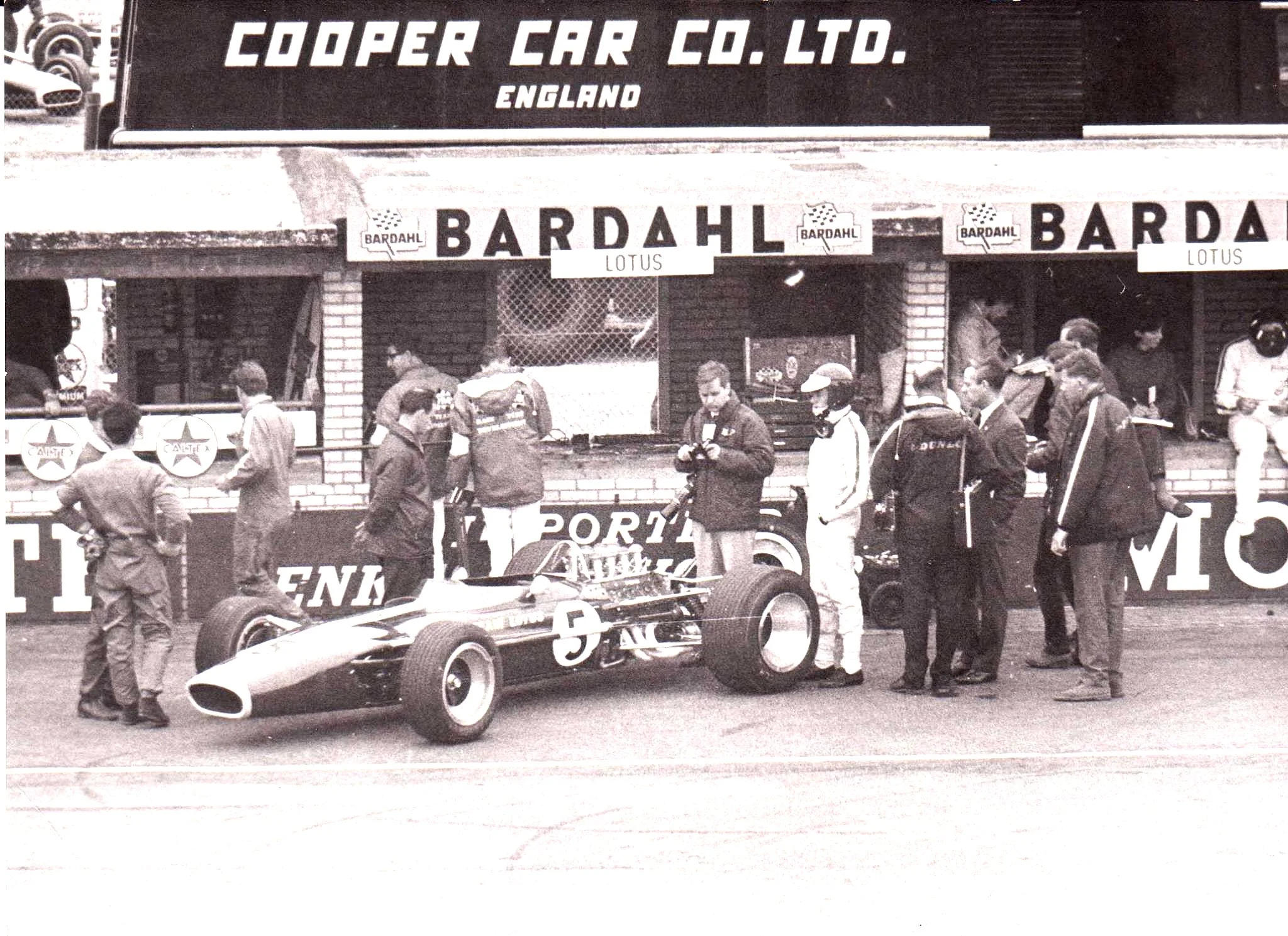 Cooper transporter was parked in the paddock behind the pits. Graham Hill sits on the Lotus pit counter on right. The picture must have been taken from the grandstands opposite.