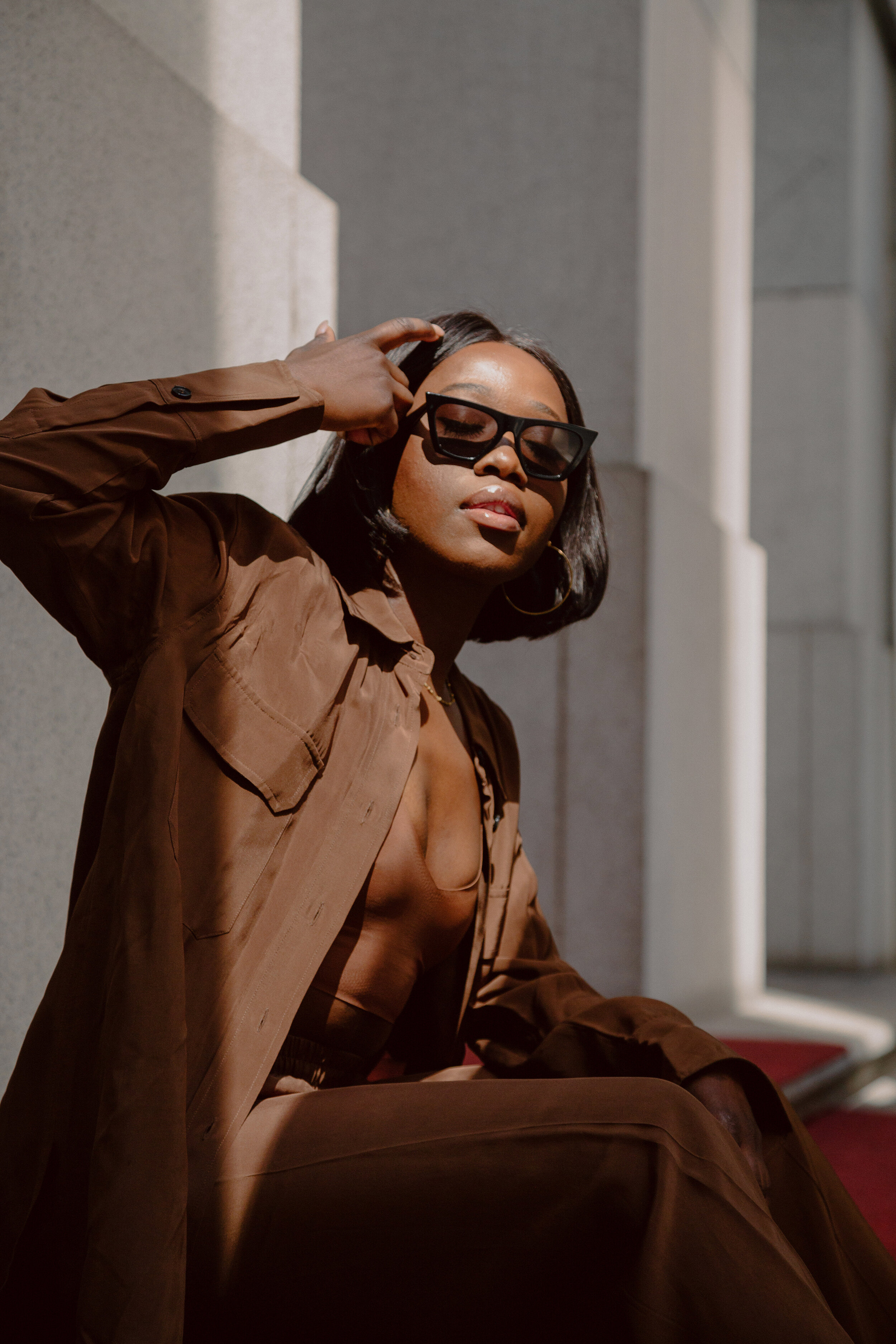 Style influencer Moyo Ayodele faces toward a patch of sunlight in a modern architectural setting