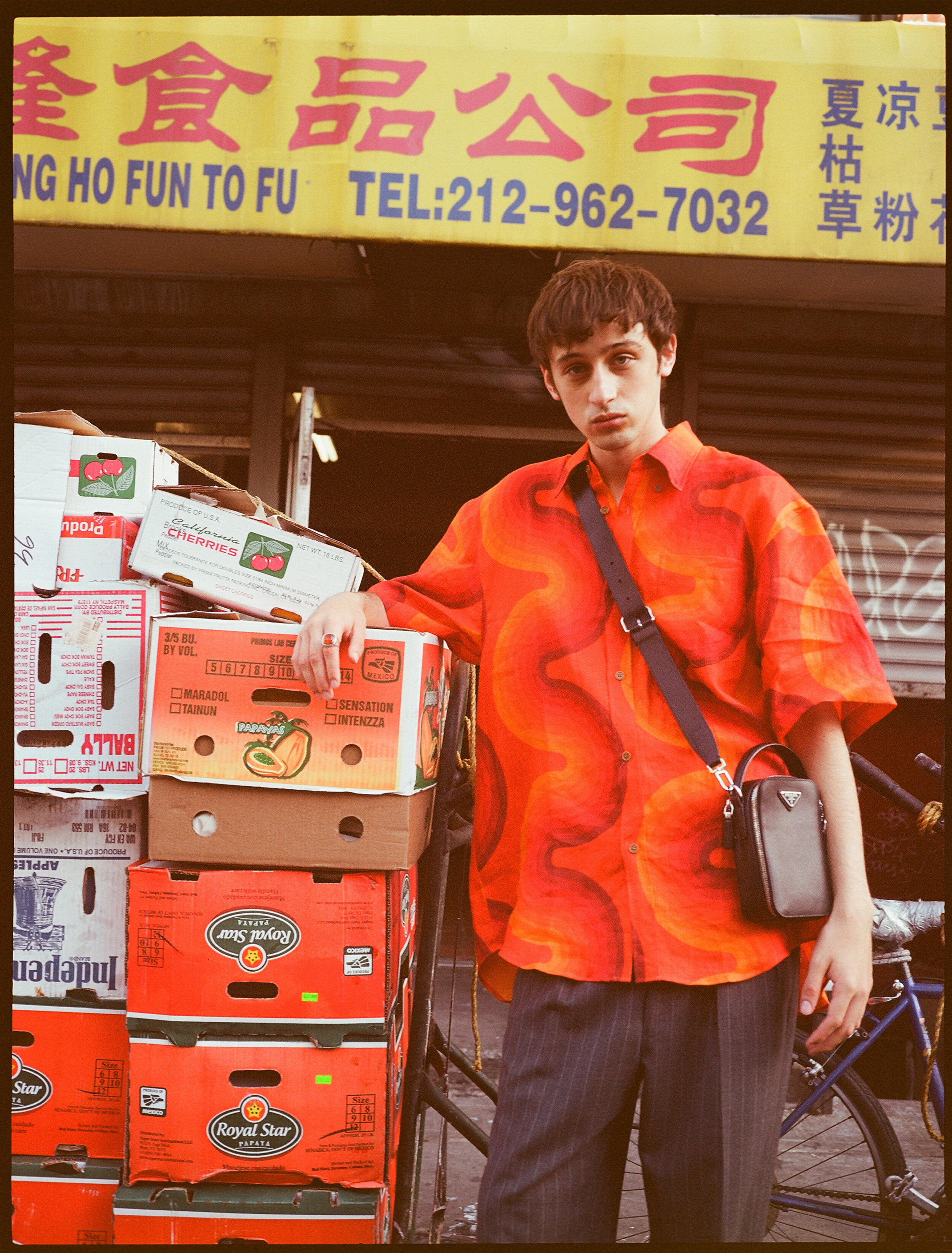 Fashion influencer Eric Jess wears a bright orange shirt next to some orange Papaya boxes in Chinatown, NYC