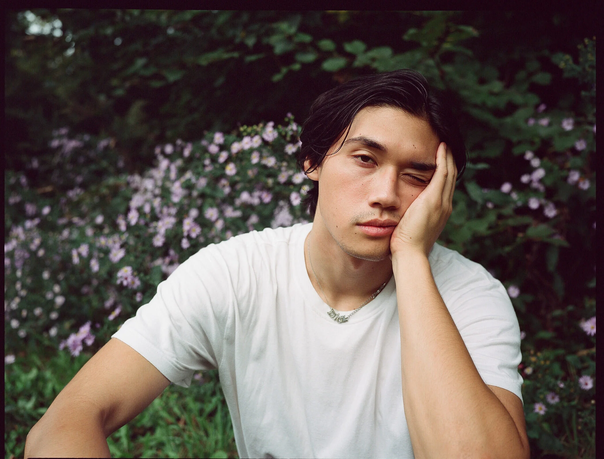 Ethan Heath sitting near a patch of lilac flowers, Prospect Park Brooklyn