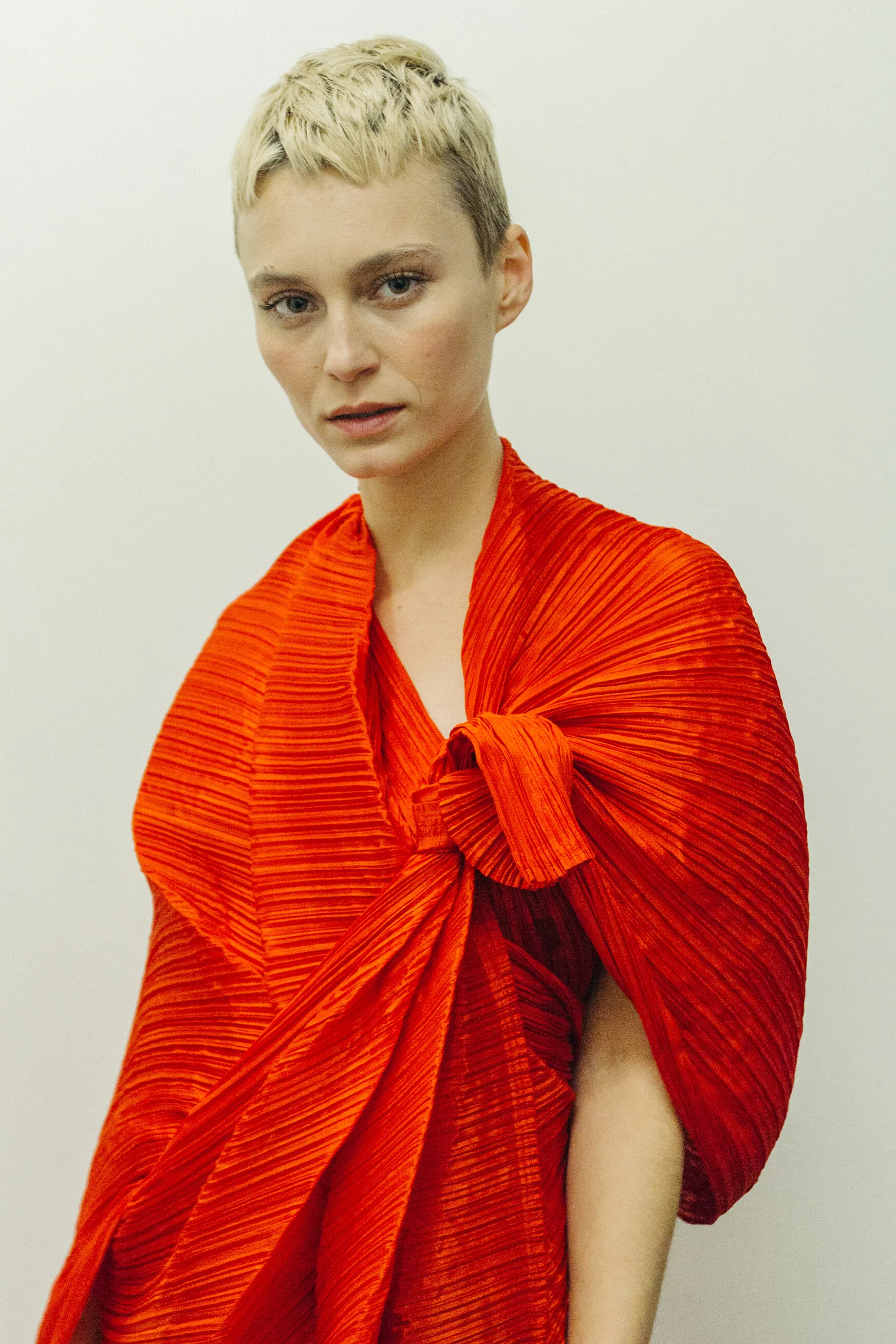 Short haired blonde woman wears a red pleated wrap dress by designer Issey Miyake