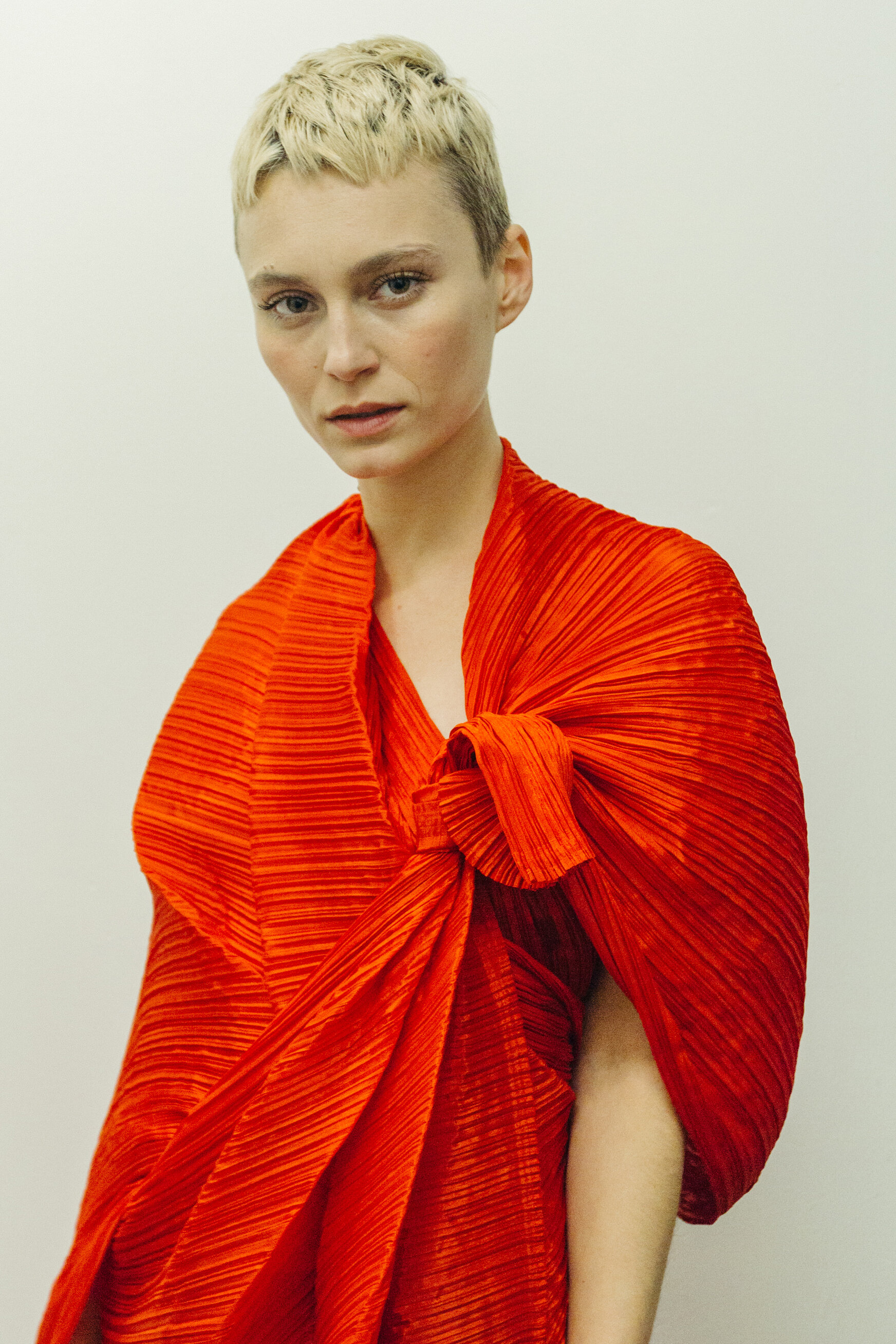 Short haired blonde woman wears a red pleated wrap dress by designer Issey Miyake