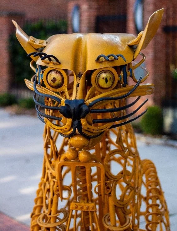 You’ll find the “Yellow Farm Cat” sculpture located on the corner of W. Gay Ave. and N. George St.