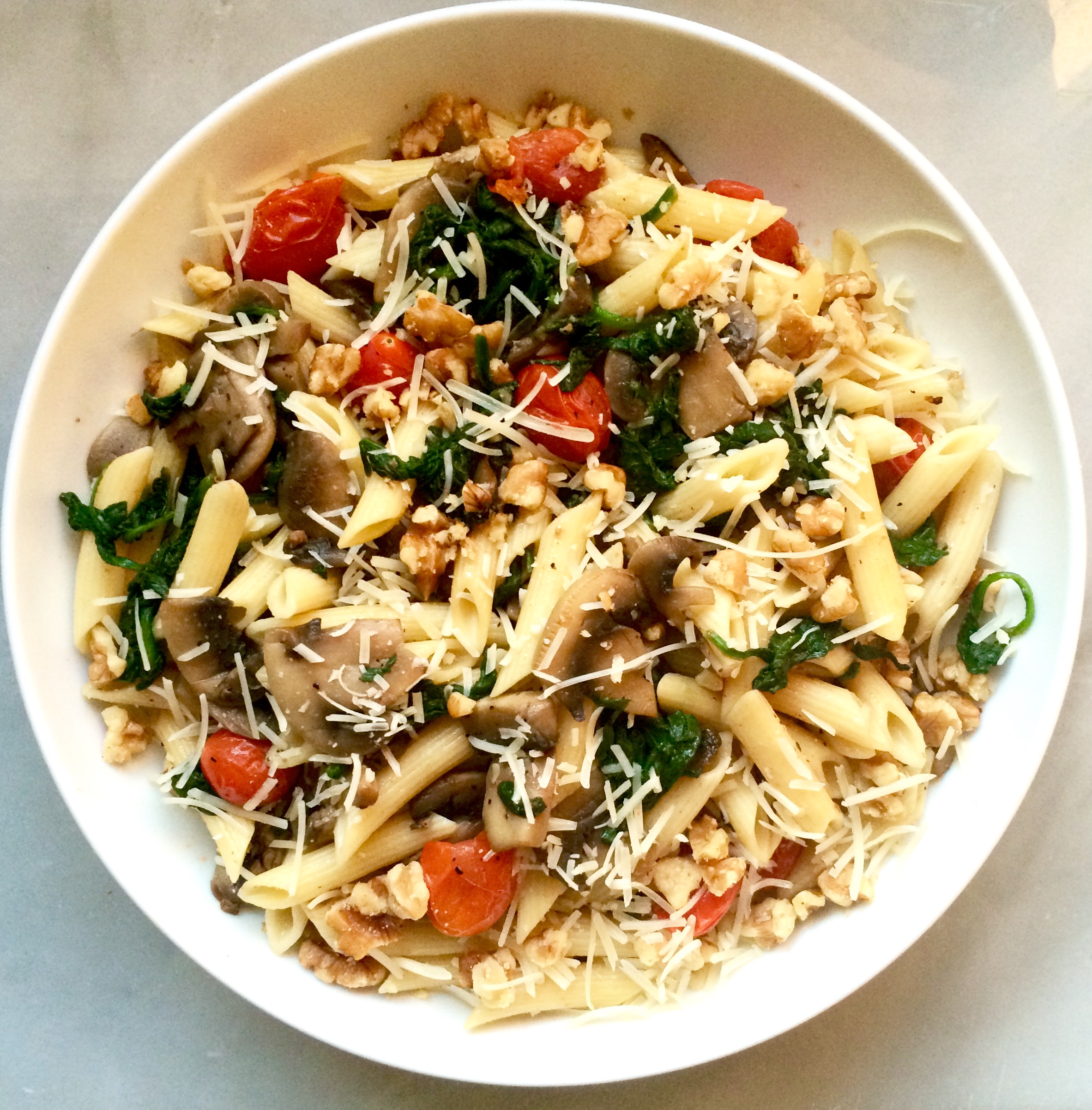  Pasta with mushrooms, spinach, and tomatoes, with a garnish of walnuts and parmesan