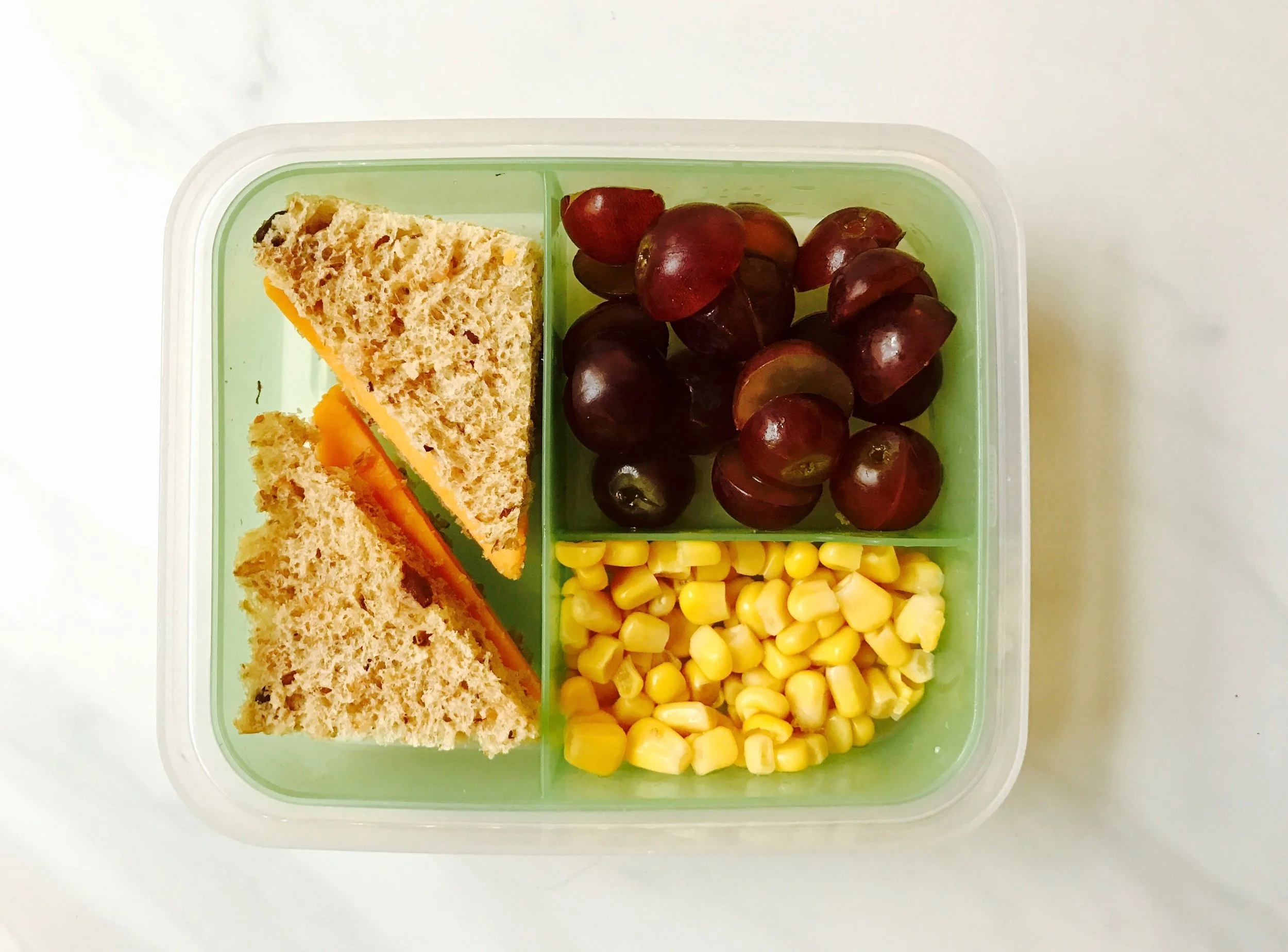 Angelic Bakehouse bread without crust (honey wheat raisin) with cheddar cheese, purple grapes, and canned corn.