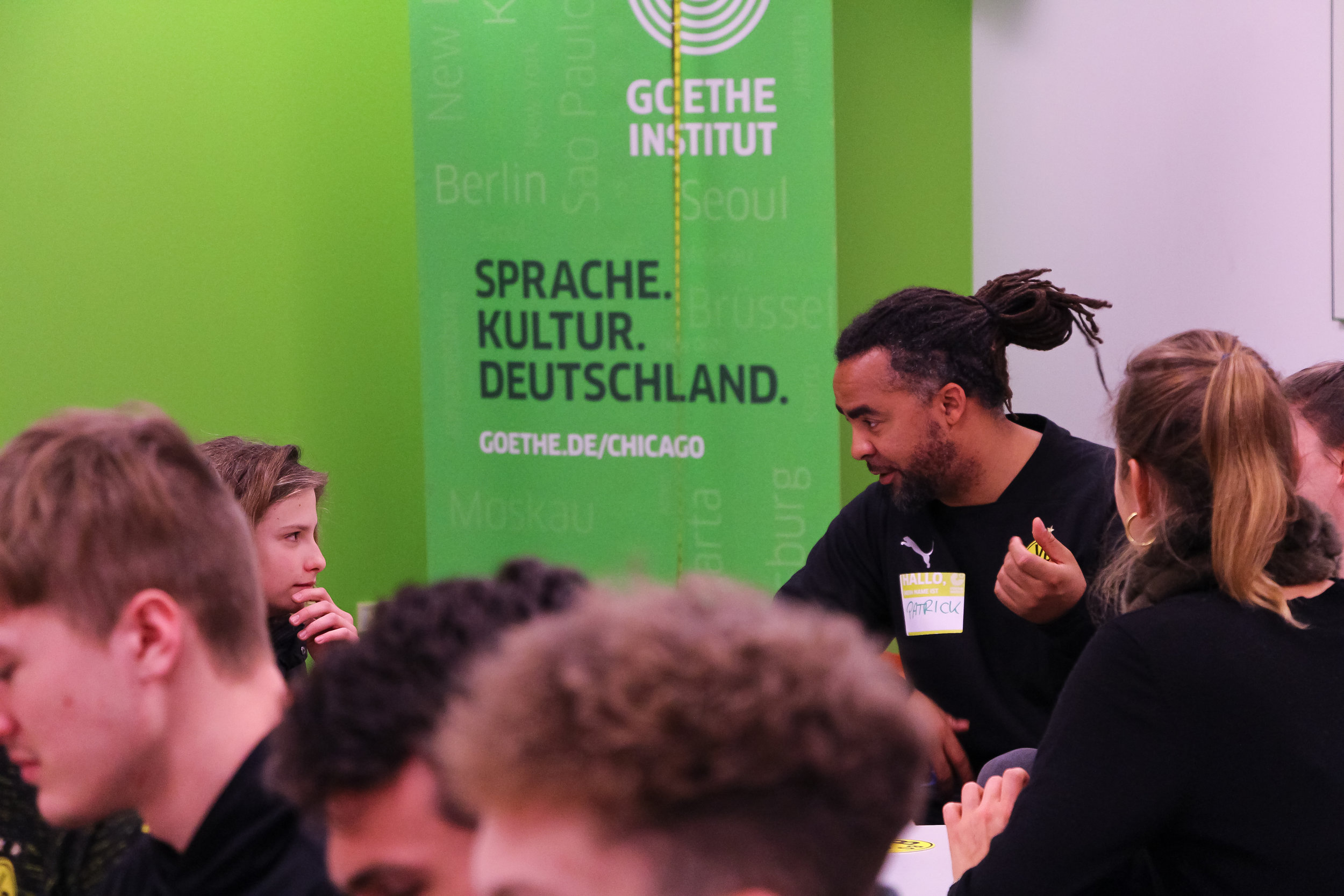  Former Borussia Dortmund and German National Football Team player Patrick Owomoyela chats with a student. Goethe-Institut, Chicago, 2019. 