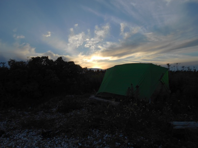 Tent with driftwood anchors on shingle at edge of beach.