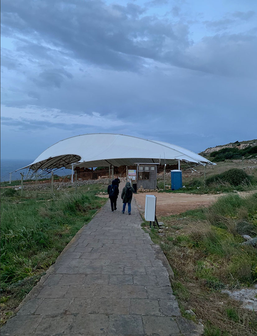  Walking down the visitors’ path to Mnajdra Temple, which is protected from the weather by a canopy. The sea is visible in the distance. 