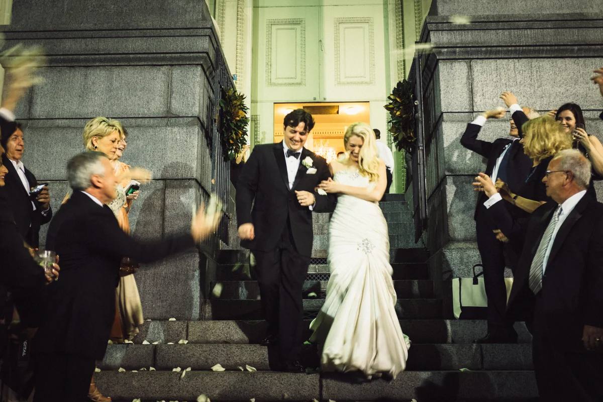 Bride and groom walking down steps at night, surrounded by family and friends throwing flower petals, celebrating their wedding.