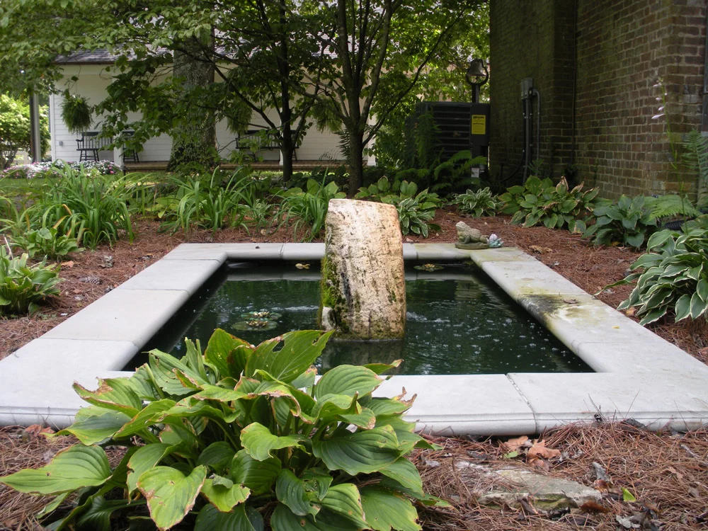 Koi pond with limestone coping and a vertical antique Millstone