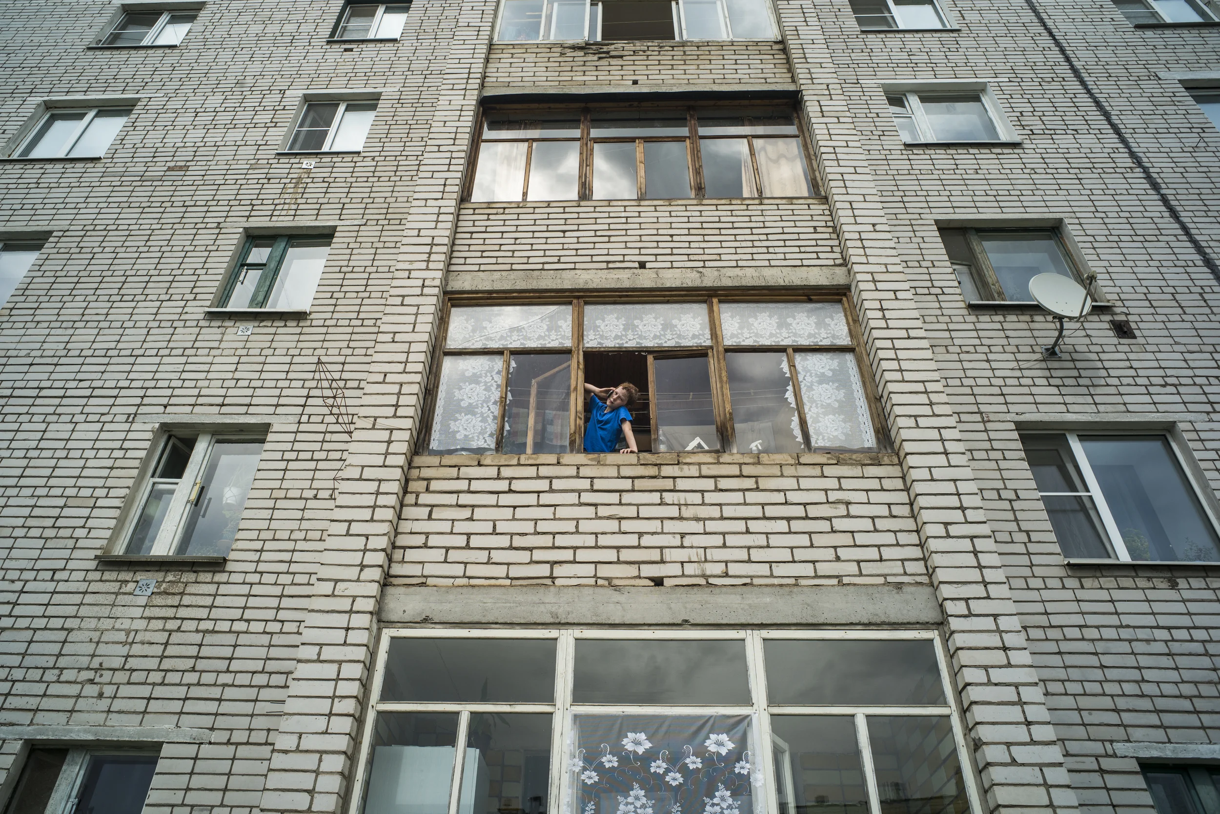 A young boy gazes out of the window of an apartment complex in the early morning of May 30, 2015 in the town of Kotlas in Arkhangelsk Oblast, Russia. (© Alicia Afshar)