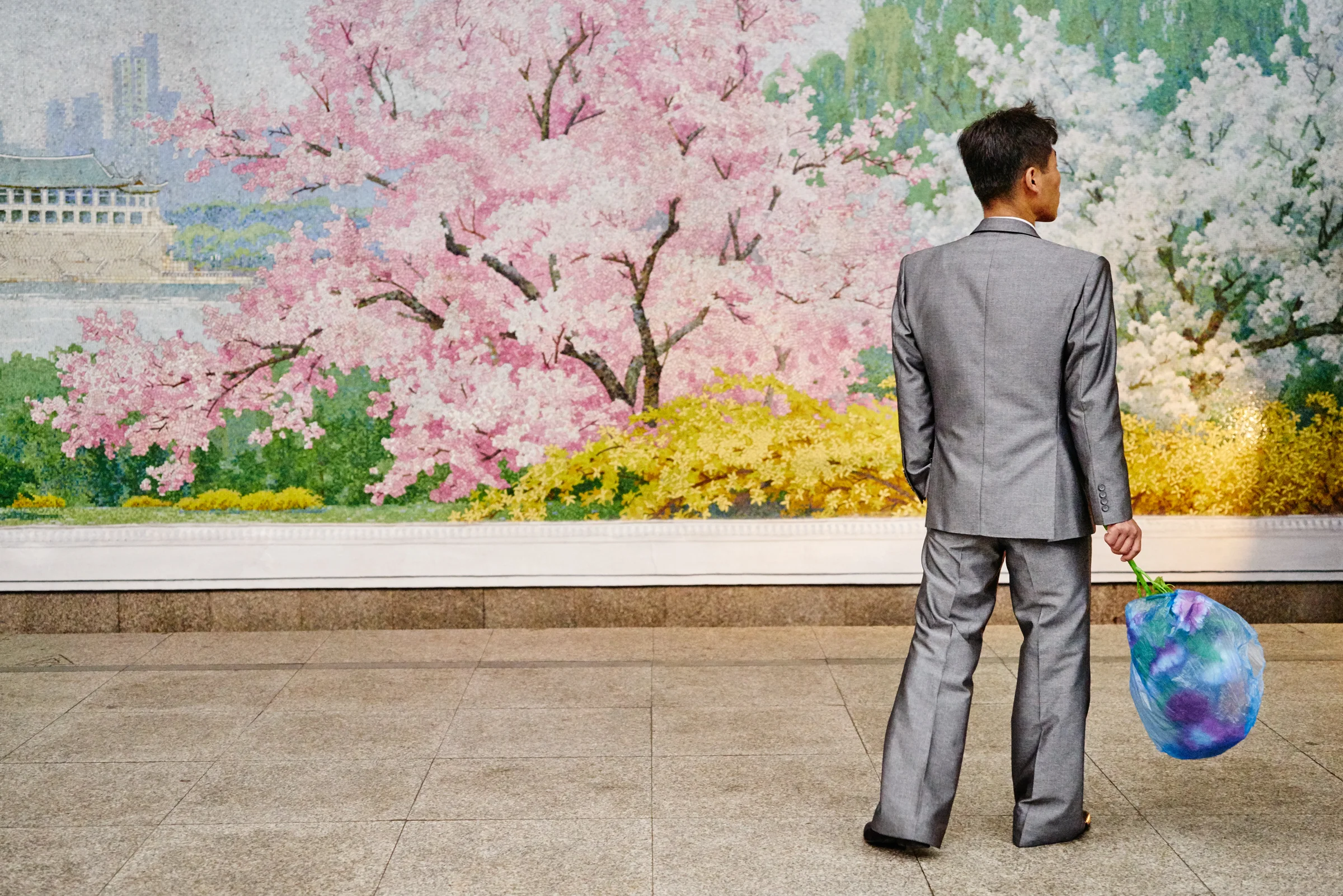 A well-dressed man waits with a bouquet of flowers at the Pyongyang Metro. 
