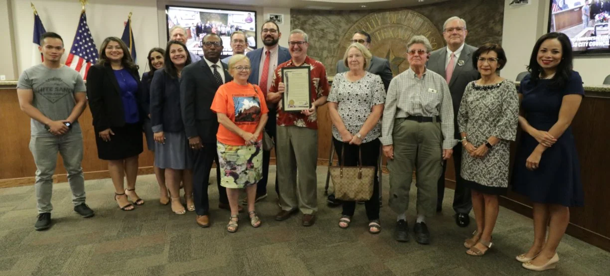 Jim Tolbert, CEO of COM, in the center holds the proclamation. To his right is Dr. Gertrud Konings. To his left, Eileen Karlsruher, COM Board Tresurer. To Eileen’s left is Carol Brown. On the far left in the picture is Pham Hao. Behind Gertrud Konin…