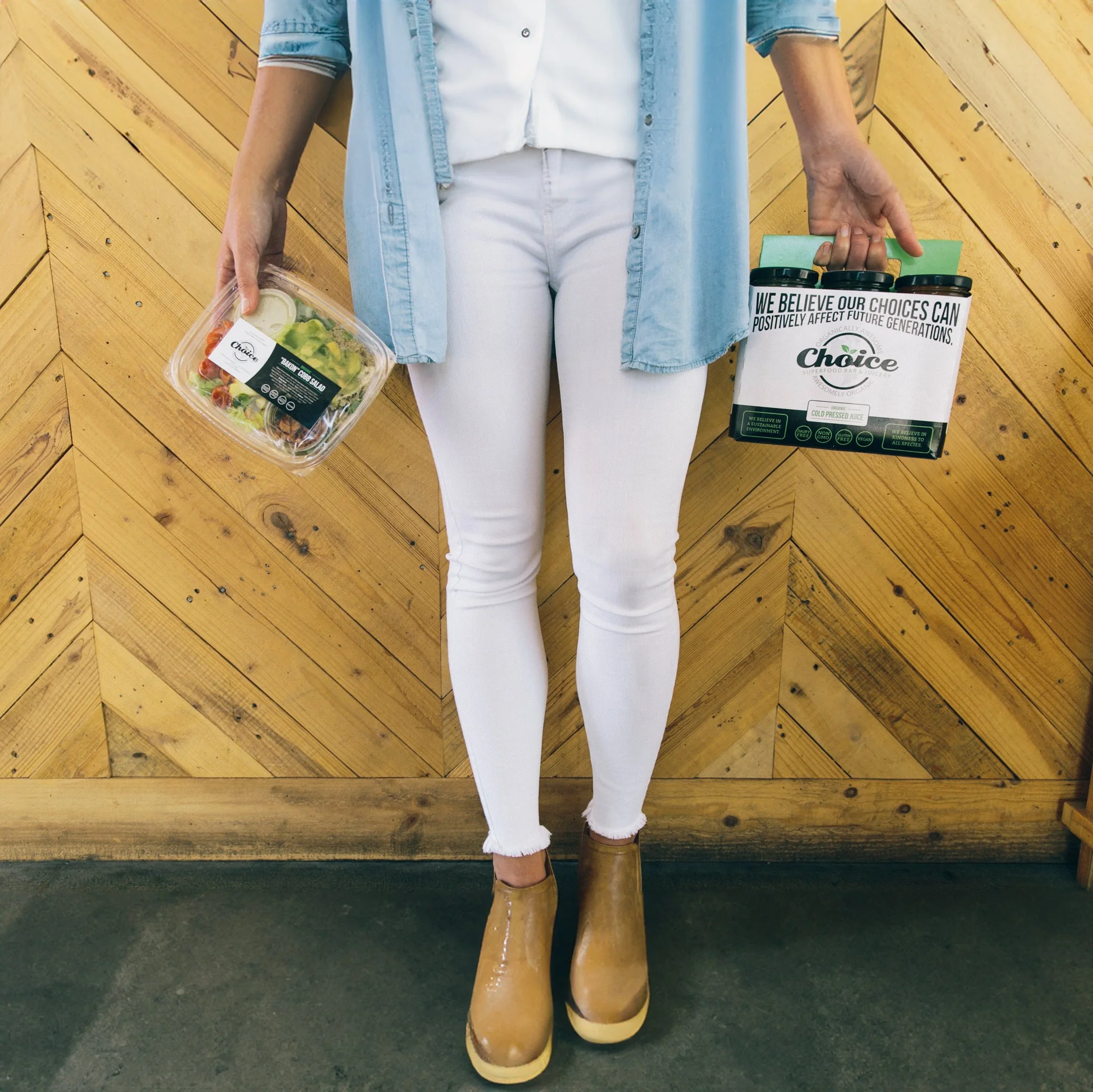 Person holding a Choice Juicery salad in one hand and a four-pack of Choice cold-pressed juices in the other.