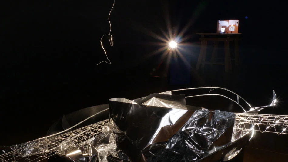 Installation view of “Automatic Vaudeville” at Pitzer College Art Galleries, 2018. Foreground: “Praxinoscope” (2018) (Partial view, still); Kinetic sculpture (16mm projector, motor, lamp, wood, metal, mylar sheeting); Dimensions variable, installation approximately 90’x90”x90”. Background: “Limelight” (2018), Video sculpture (single channel video, wood, paper, metal, candle lamp; 30”x30”x60”; 4:20 Installation view: Automatic Vaudeville at Pitzer College Art Galleries (2018) Left: Praxinoscope (2018) (Partial view, still) Kinetic sculpture (motor, wood, metal, mylar sheeting) lamp, 16mm projector Dimensions variable, installation approximately 90” x 90” x 90” Right: Limelight (2018) Single channel video, wood, paper, metal, candle lamp 30” x 30” x 60”, 4 min 20 second video