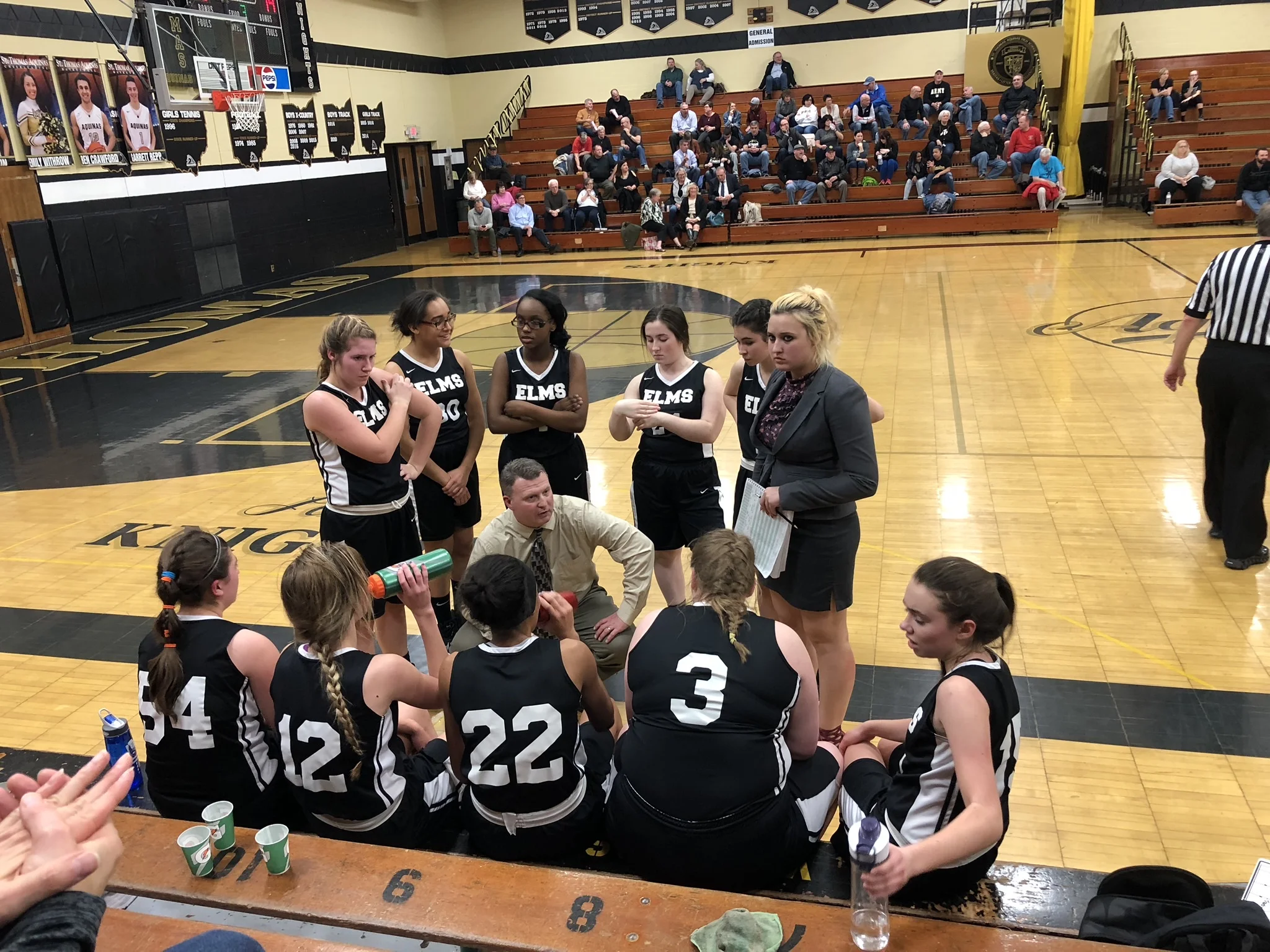 Members of the Elms Varsity Basketball Team discuss strategies with their coaches during a season game.