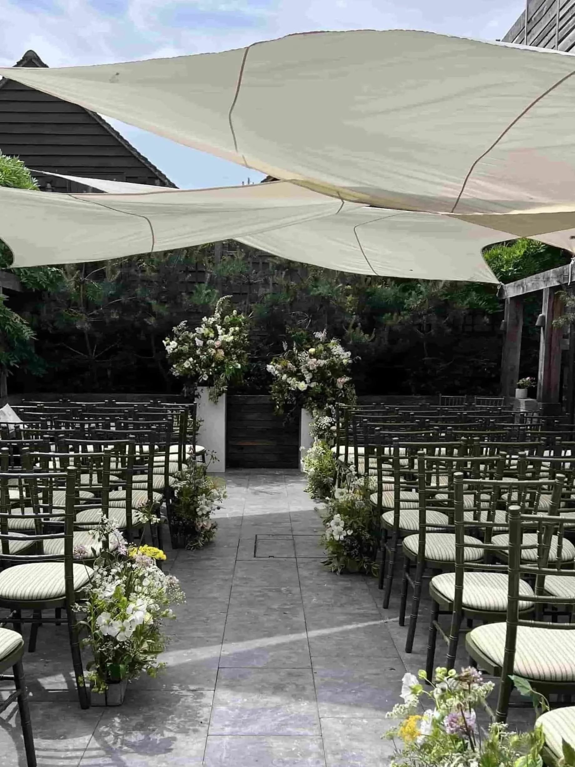 A courtyard wedding set up at The George in Rye, featuring Aisle flowers framing the aisle and leading to the Floral ceremony where the couple will take their vows