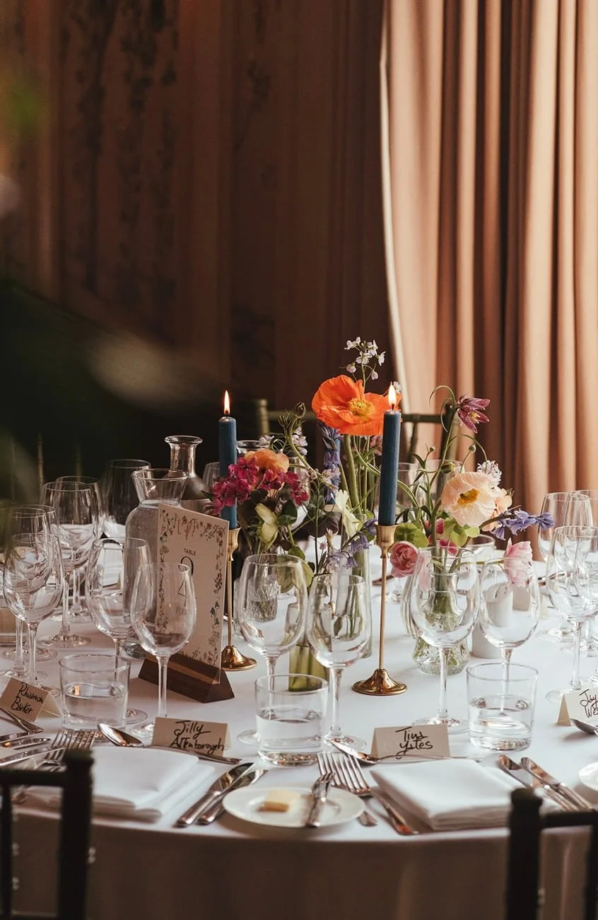 the picture shows a round table set up in the George Ballroom, simple bud vases grouped together with candles and candlesticks, is a popular choice when choosing wedding flowers at The George in Rye
