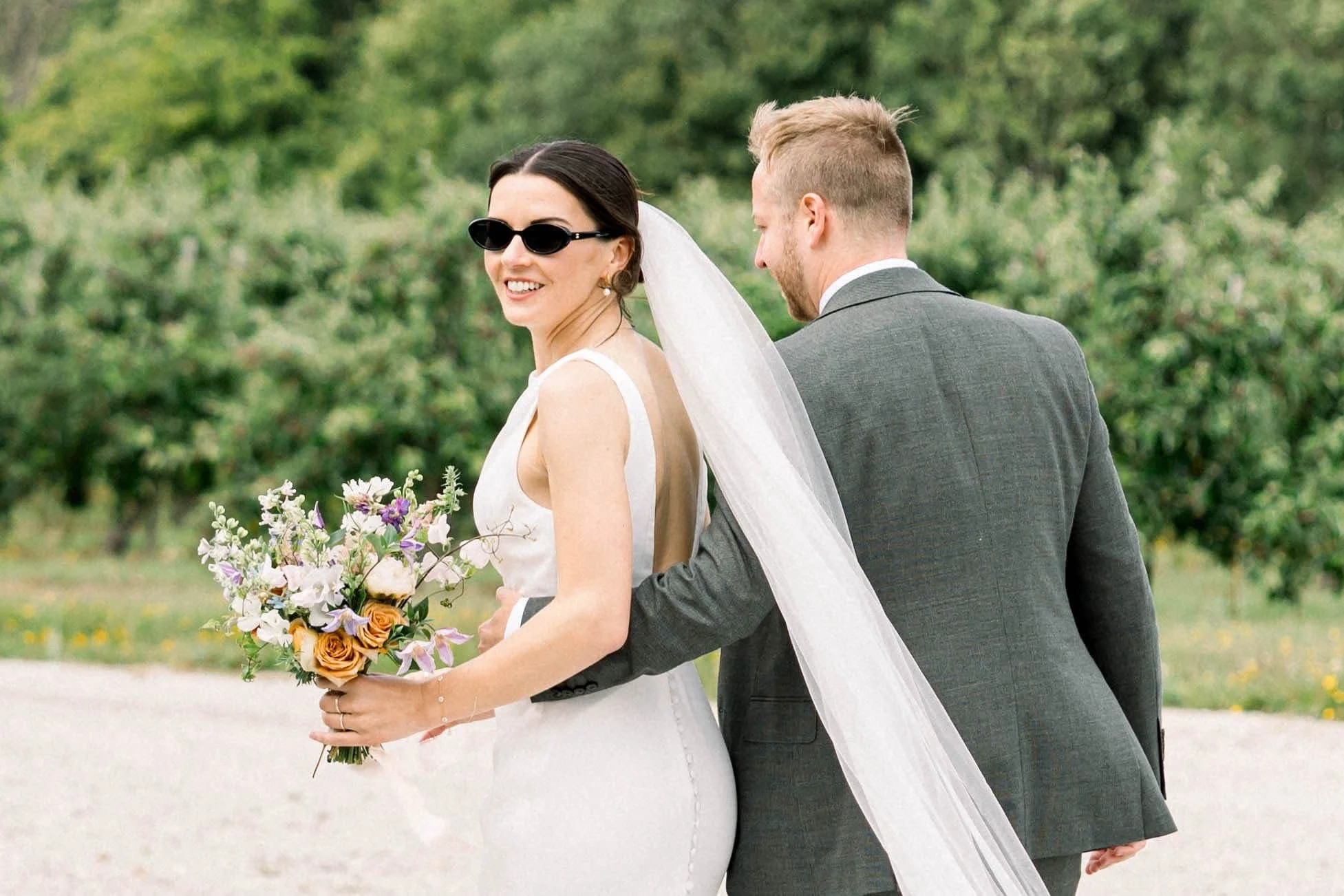 this image shows a happy bride and groom, the bride is wearing sunglasses which show that the sun did come out, and after a rainy start, it didnt ruin their day