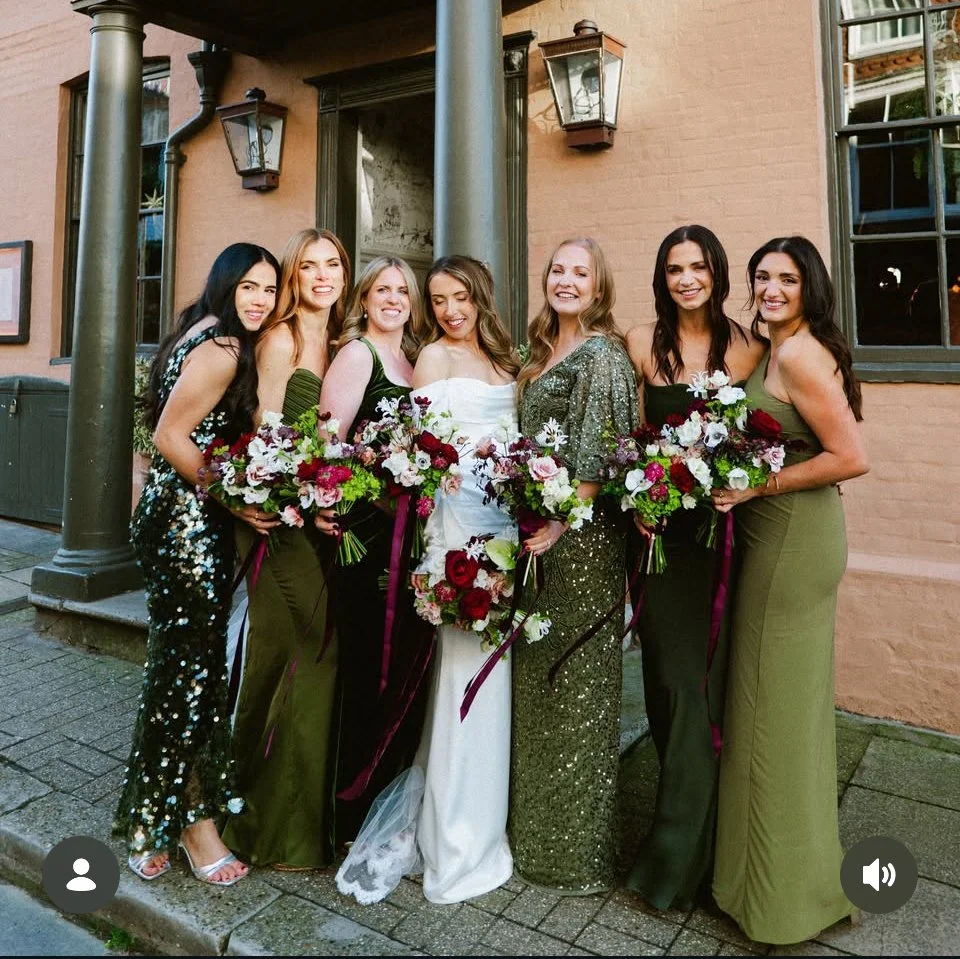 Winter wedding at the George in Rye, the image shows the bride and her 6 bridesmaids in different green dresses, holding modern burgundy, white and green bouquets