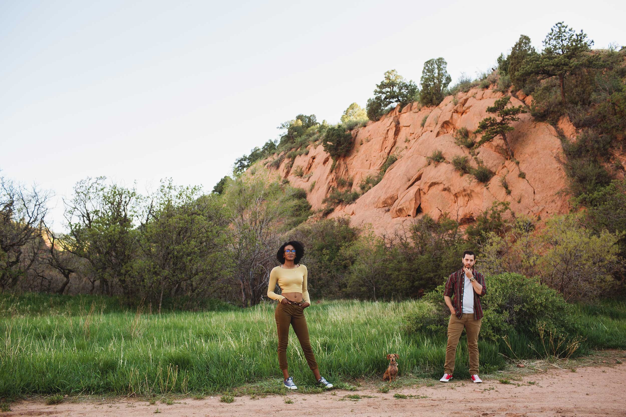 outdoorsy mixed couple with their little brown dog standing in front of a meadow at red rocks canyon open space in Colorado Springs