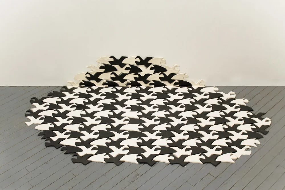 Fish/Bird E34B , 2013, 211 glazed ceramic tiles, 20 x 70 x 60 in. Fish/Bird E34B is a floor/wall piece made out of 211 glazed ceramic tiles. It is based on M.C. Esher’s piece from his group “Symmetry Drawings”. Formally, the sculpture is compiled from tessellated shapes of birds and fish, which fit into each other like a jigsaw puzzle. Mimicking the original, the bird and fish tiles alternately function as foreground or background, depending on whether the eye focuses on light or dark elements. 