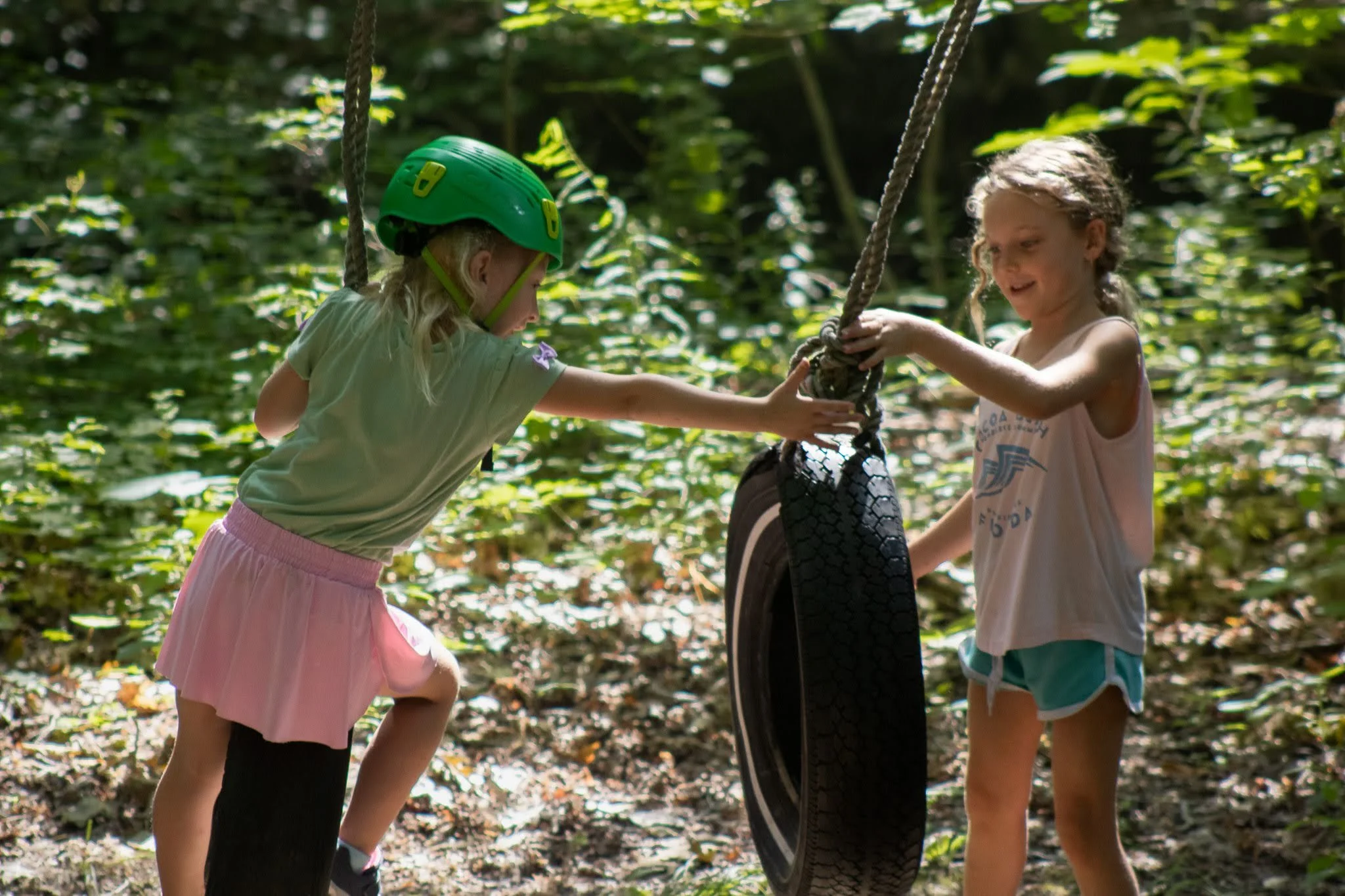 Two campers help each other at a tire swing in the woods.
