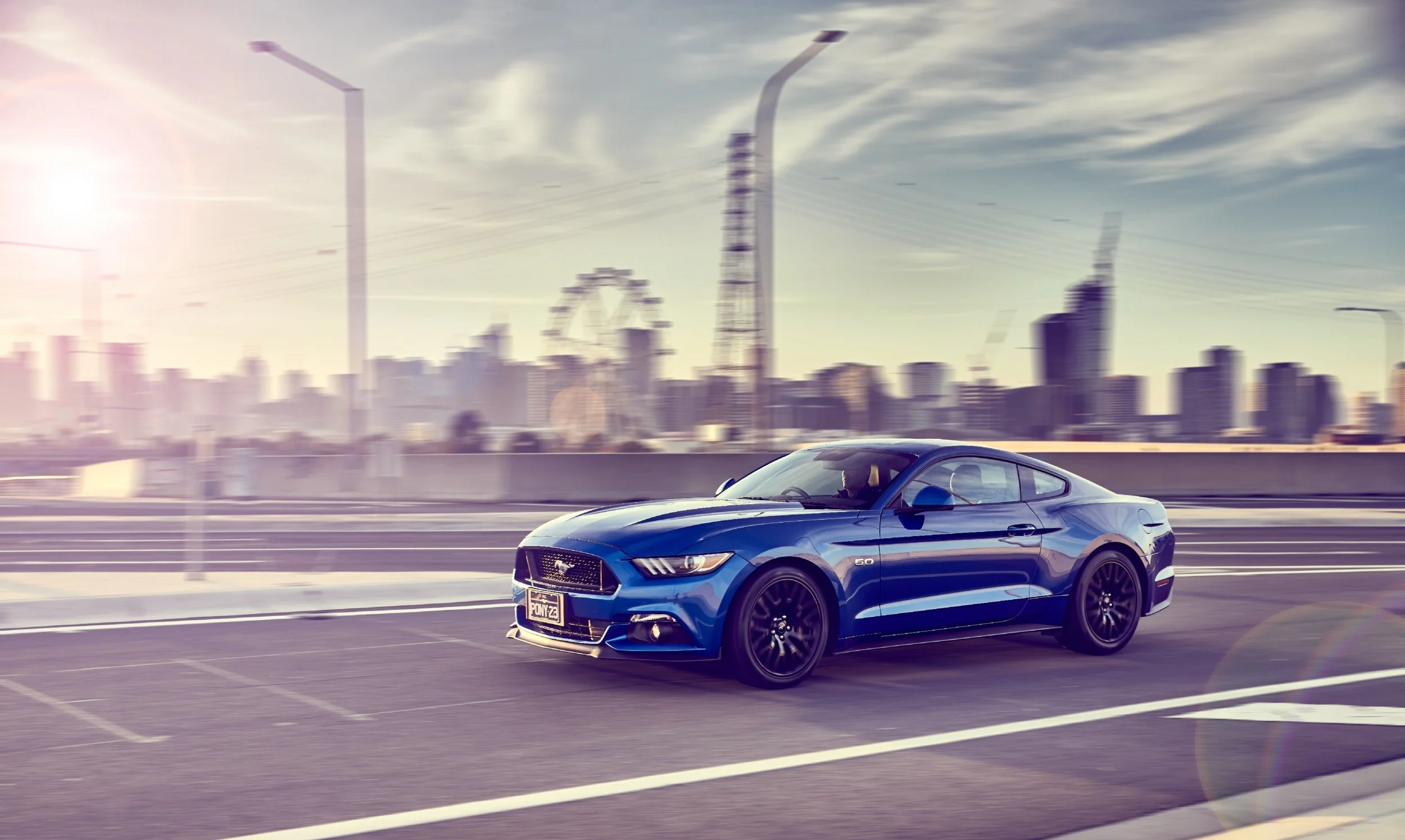 This is a picture of a blue 2017 Mustang GT going around a corner at dawn with the city in the background. Photographed by a melbourne car photographer