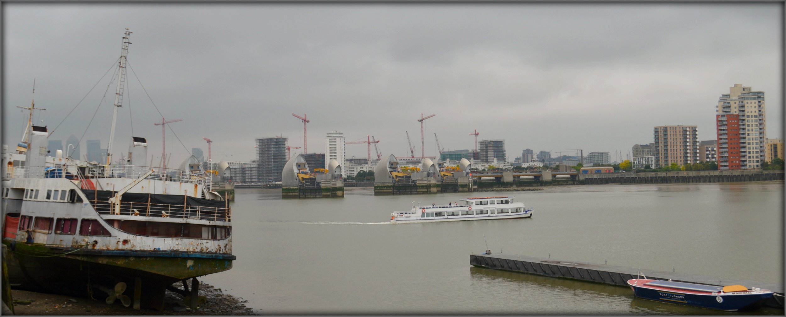 Throughout history the Thames has been central to much of London's industrial growth. This view from Woolwich outside Thames-Side Print Studio looking up towards the Thames Barrier is reflective of the many majestic and important architectural sites throughout London, and the ongoing development which we can see from the skyline of cranes & the financial powerhouse of Canary Wharf to the left. 