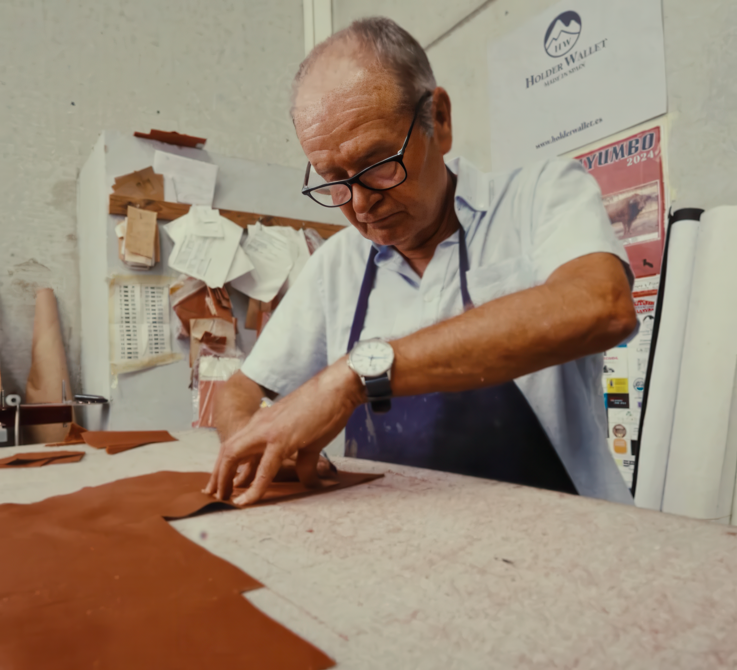 Documentary-style lifestyle photograph of a male artisan in an apron carefully cutting brown leather at a workshop table for Wolves Call handbags.