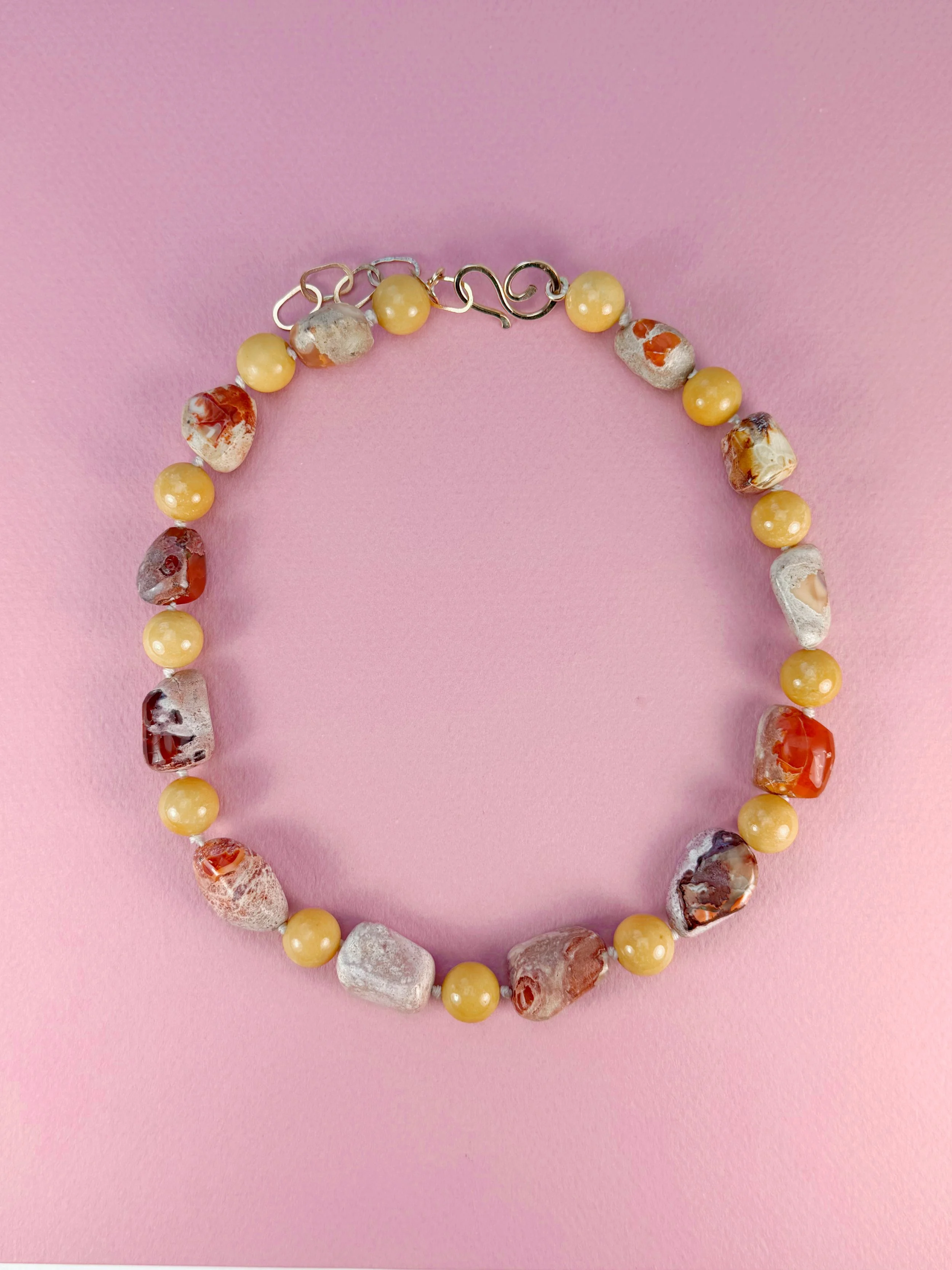 Mexican opals and yellow jade stone bead necklace on pink background