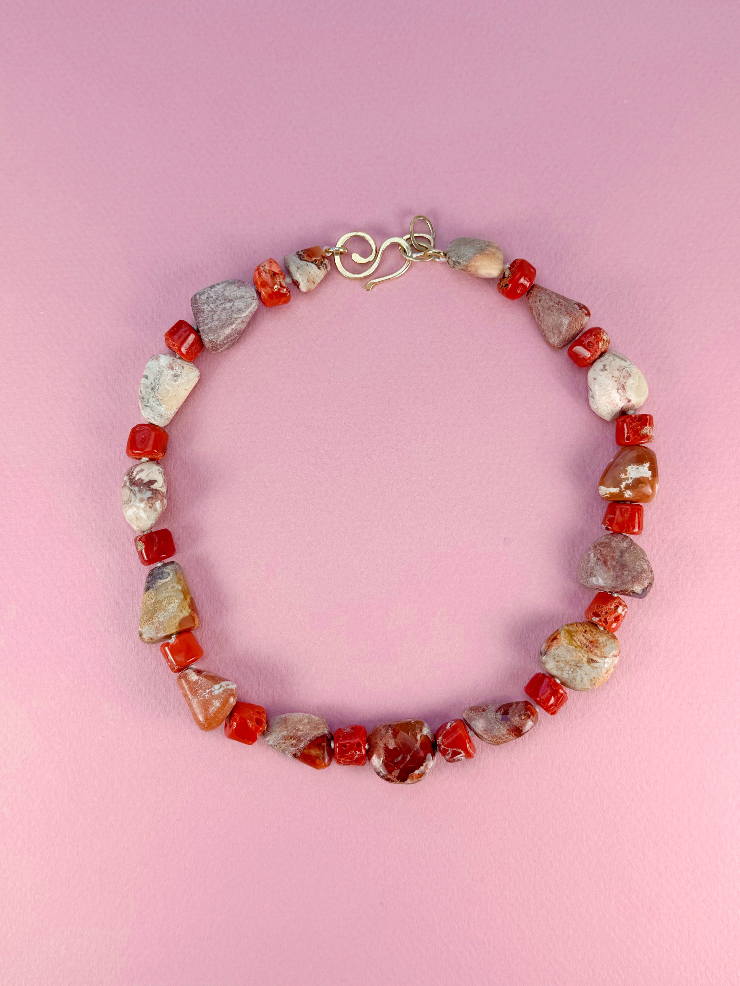 Mexican opals and raw red coral stone bead necklace on pink background