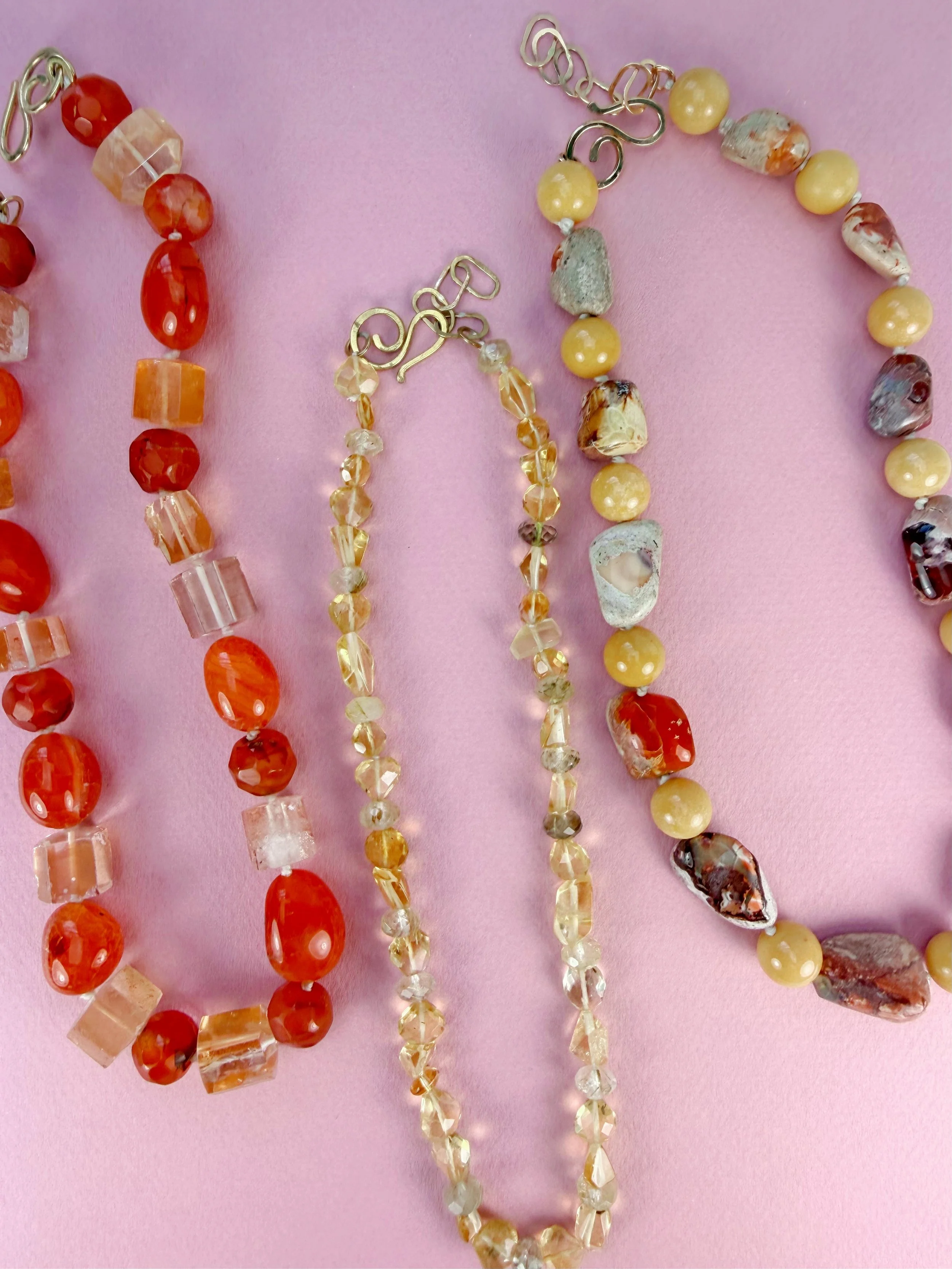 three yellow semiprecious stone bead necklaces on pink background