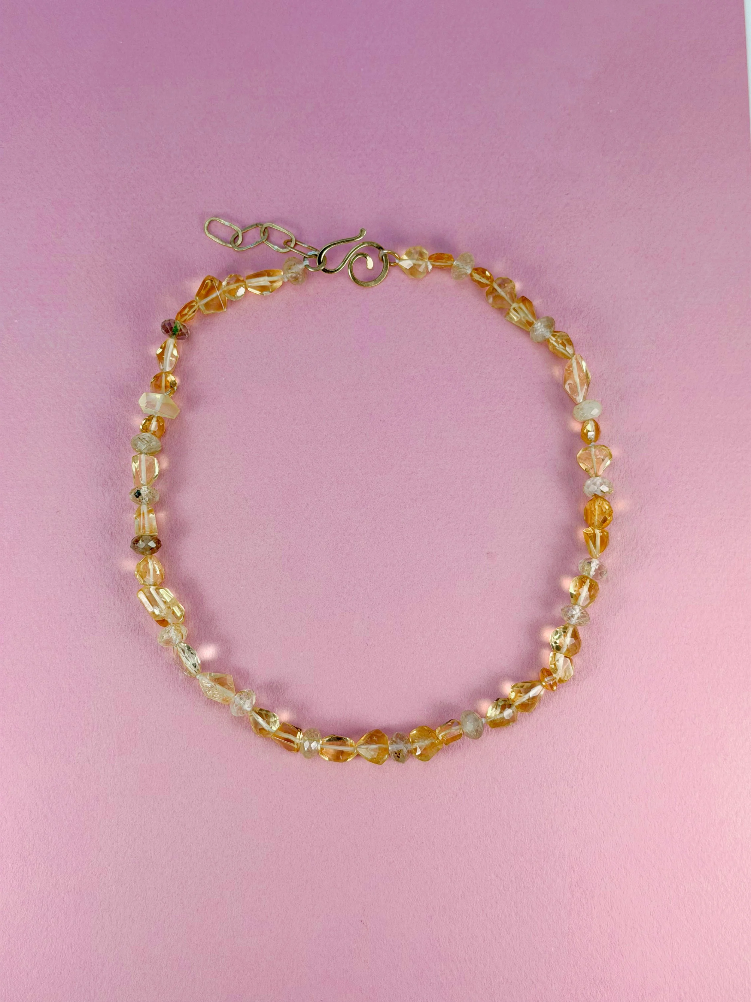 Citrine and rutilated quartz stone bead necklace on pink background