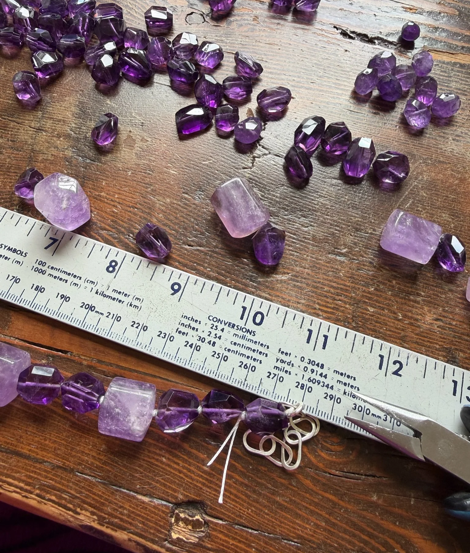 Loose amethyst stone beads and a yard stick with jeweler's pliers