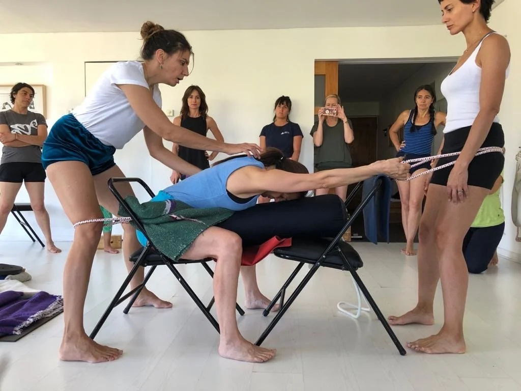Senior Iyengar Yoga Teacher Lara Warren giving an adjustment to a student on a forward bend.