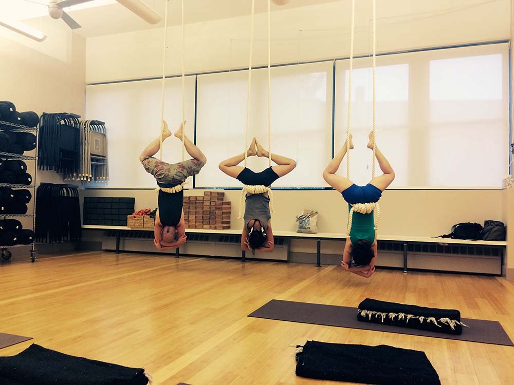 Three of Lara Warren's yoga students hanging from the ceiling ropes at the Iyengar Yoga Institute Brooklkyn.