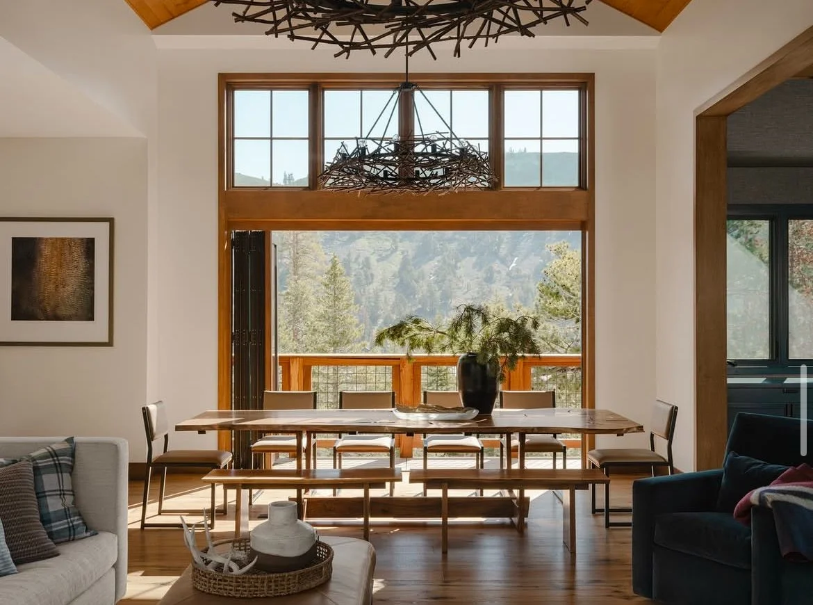 Custom Lake Tahoe dining table in a modern mountain home, handcrafted from solid wood and paired with minimalist chairs, set before expansive windows overlooking pine forests and the Sierra Nevada mountains in Kirkwood, California.