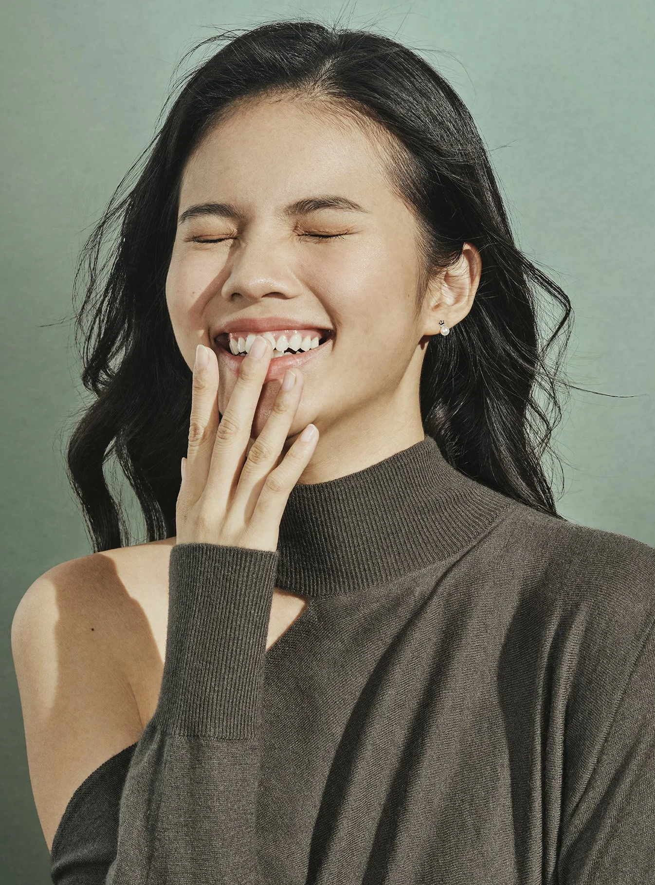 Asian woman in dark turtleneck laughing against grey-green background, Da Song campaign — Victor Marvillet photographer
