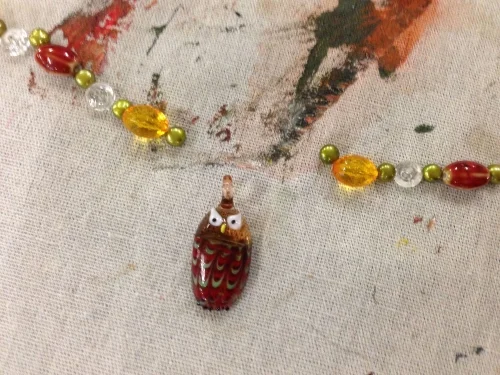 Shandell creates a pattern of beads for his wise owl necklace. 