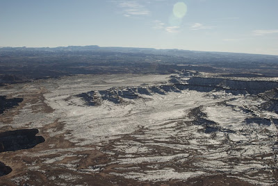 Photograph from the Grand Valley Trail, at the southern end of the Island in the Sky mesa in Canyonlands National Park. The canyon walls at the convergence of the Colorado and Green Rivers are visible beyond the rock shelf that dominates the image. The snaking line at the left is a road that follows the famous White Rim trail.