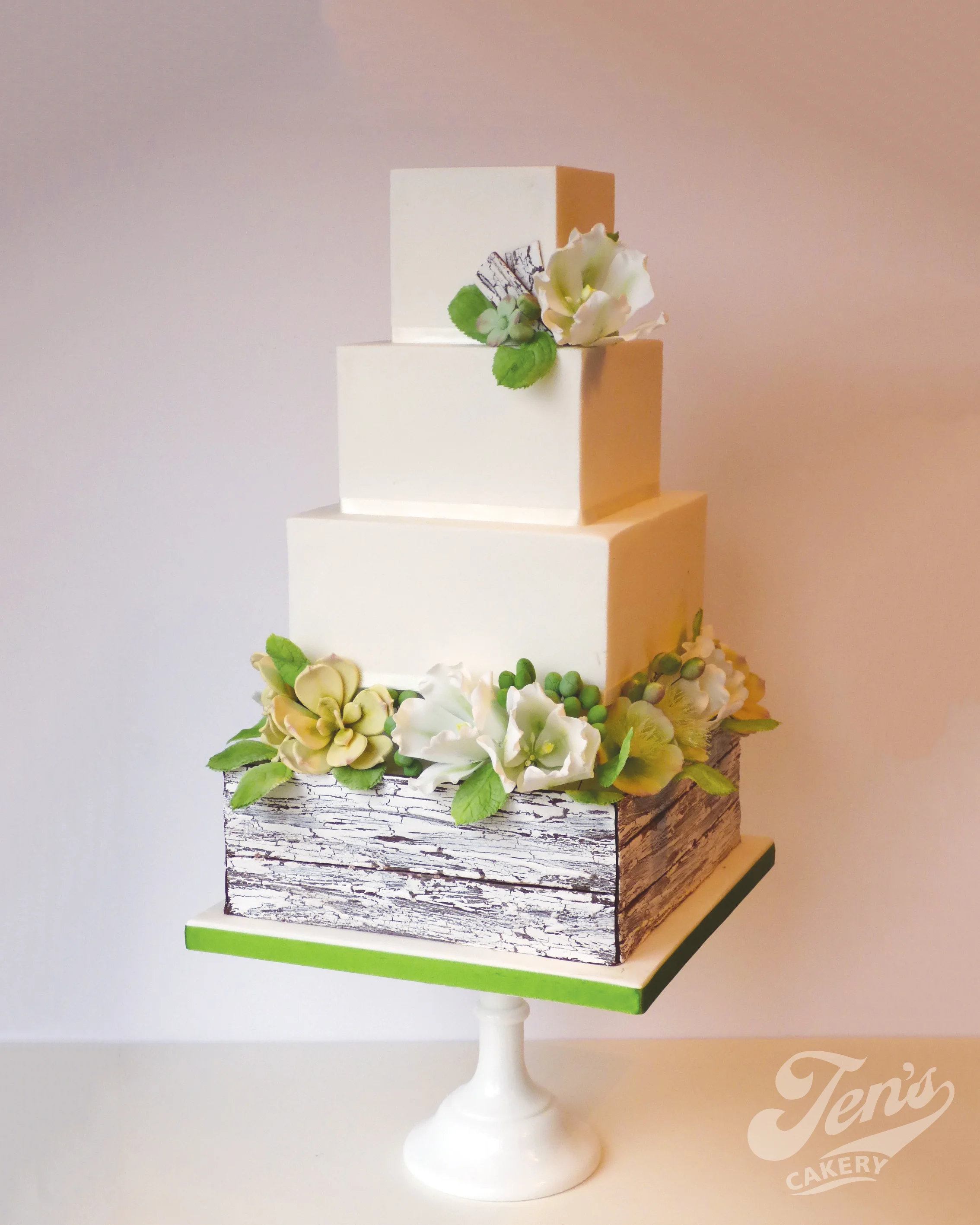 A square wedding cake with distressed painted crate, greenery foliage and sugar flowers.
