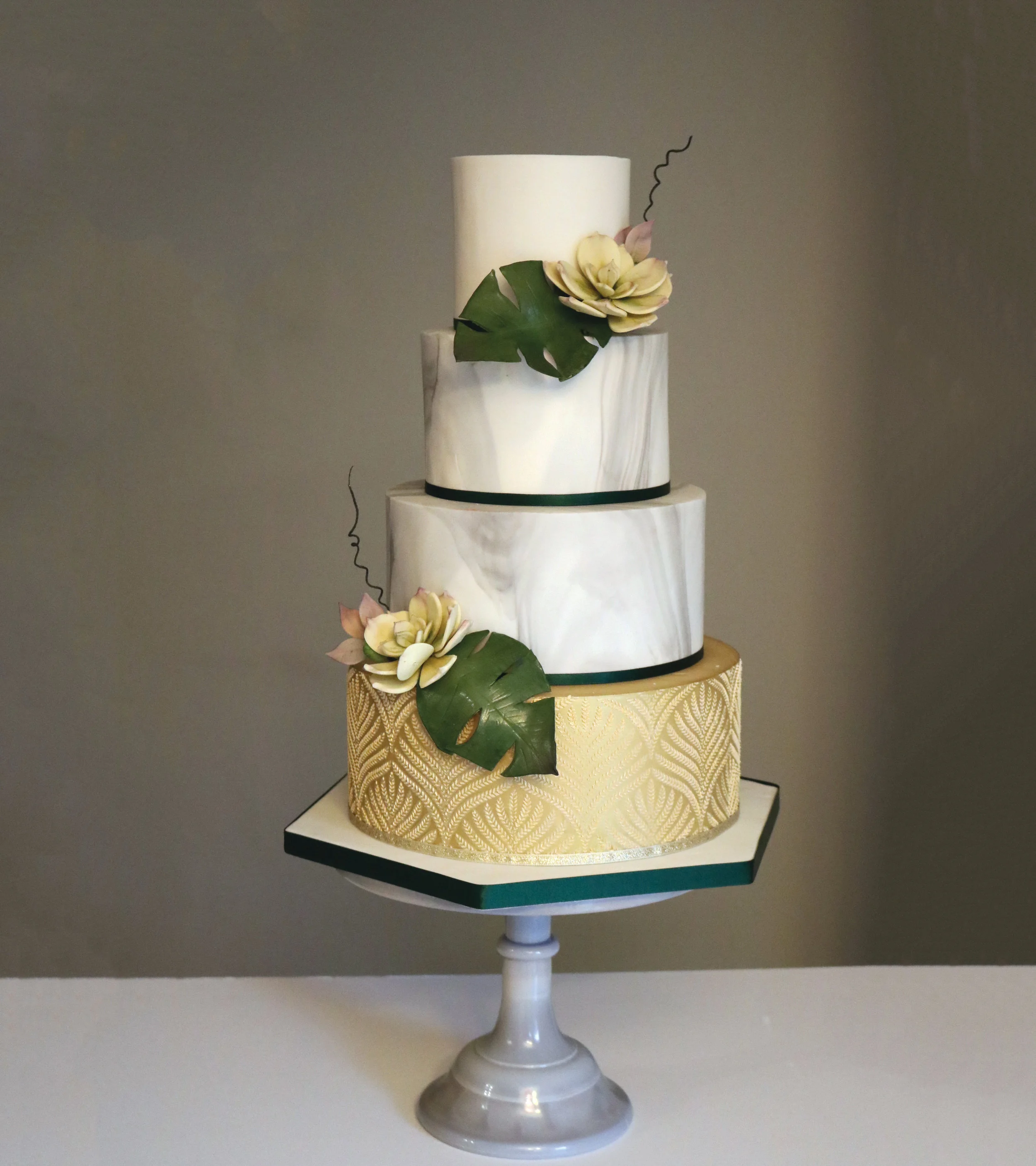 A modern wedding cake with marble tiers and gold textured tier, and decorated here with botanical or tropical leaves and flowers