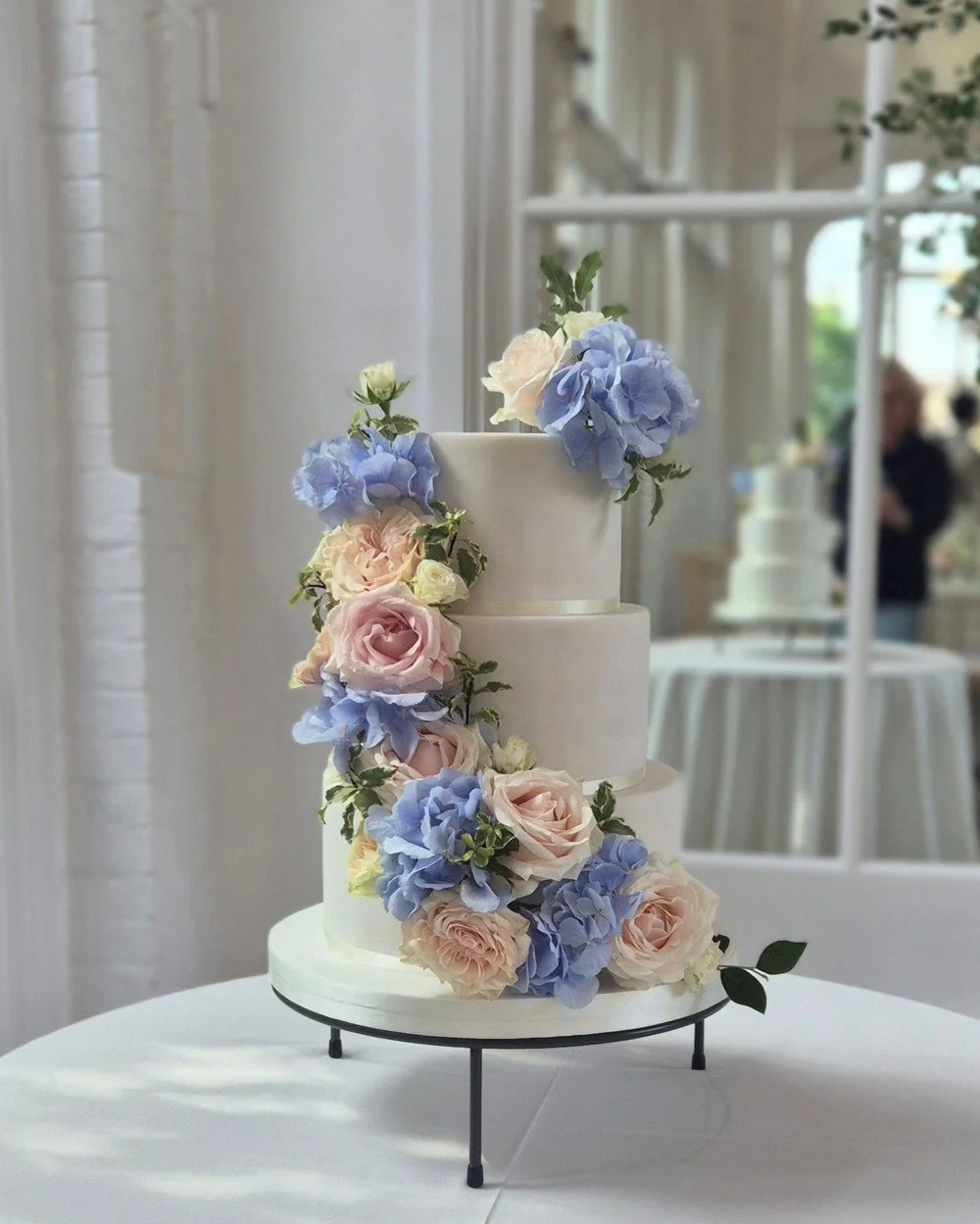 3 tier wedding cake with cascade of fresh flowers in pink and blue at the Orangery in Holland Park