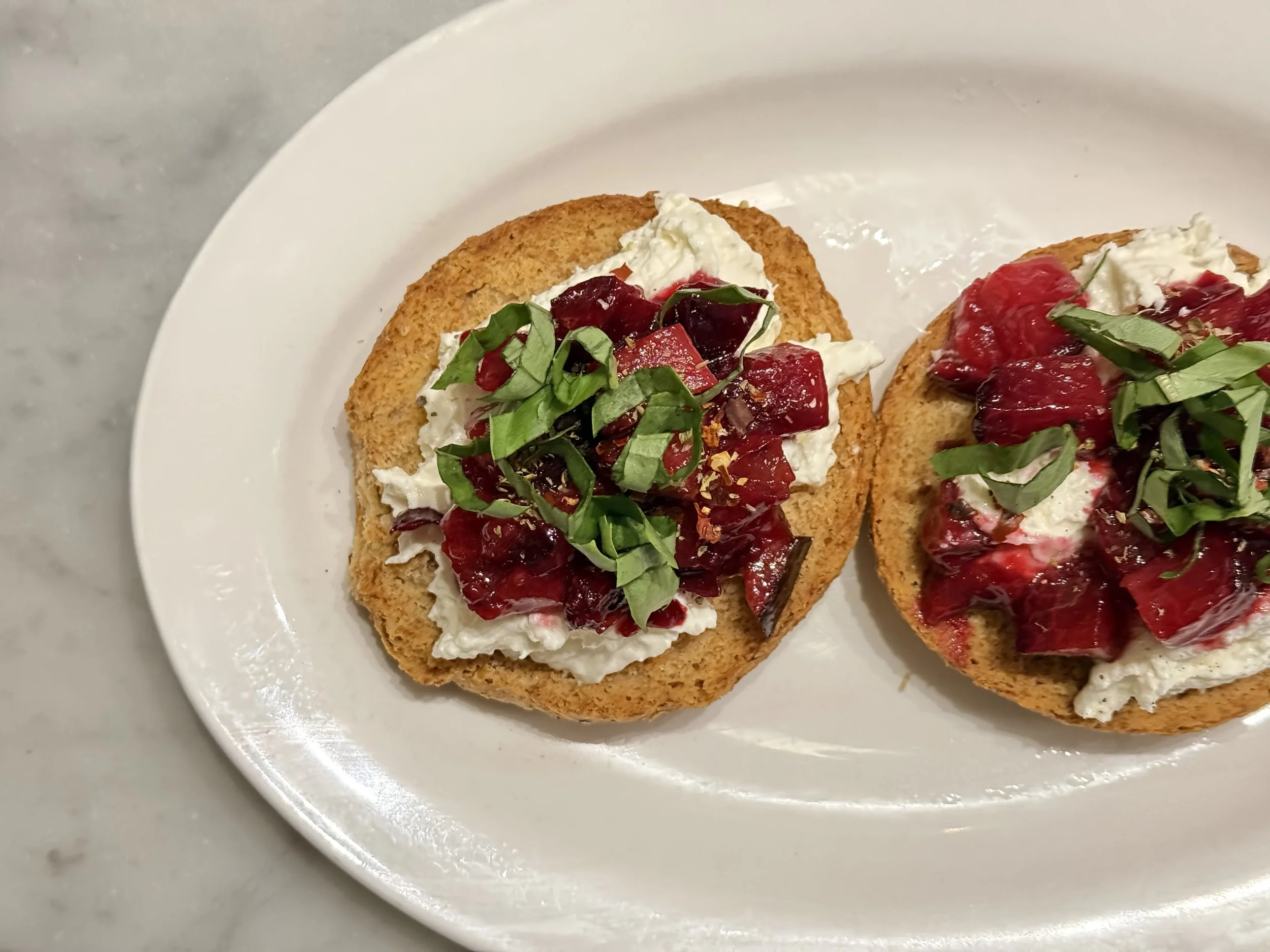 Frisella Pugliese - Two pieces of special double-backed semolina bread topped with whipped burrata, local plums, and finely cut basil