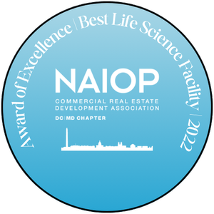 Blue circular badge with white text, reading 'Award of Excellence | Best Life Science Facility | 2022'. Centered logo with 'NAIOP' and 'Commercial Real Estate Development Association' text, and 'DC MD Chapter' underneath.
