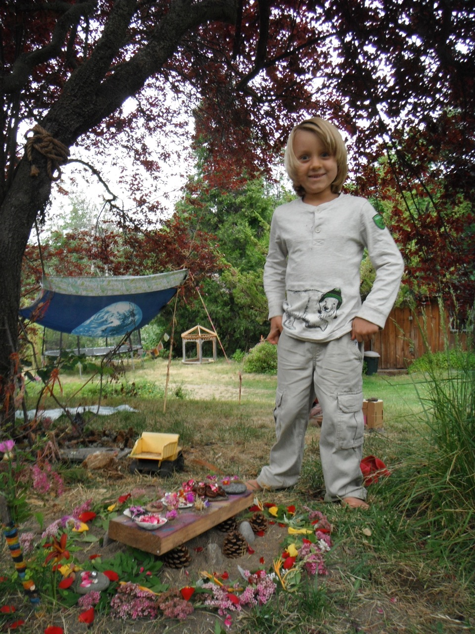 Paz age 4, with a Fairy Feast prepared by us, outside our Mother Earth Flag fort, 2014